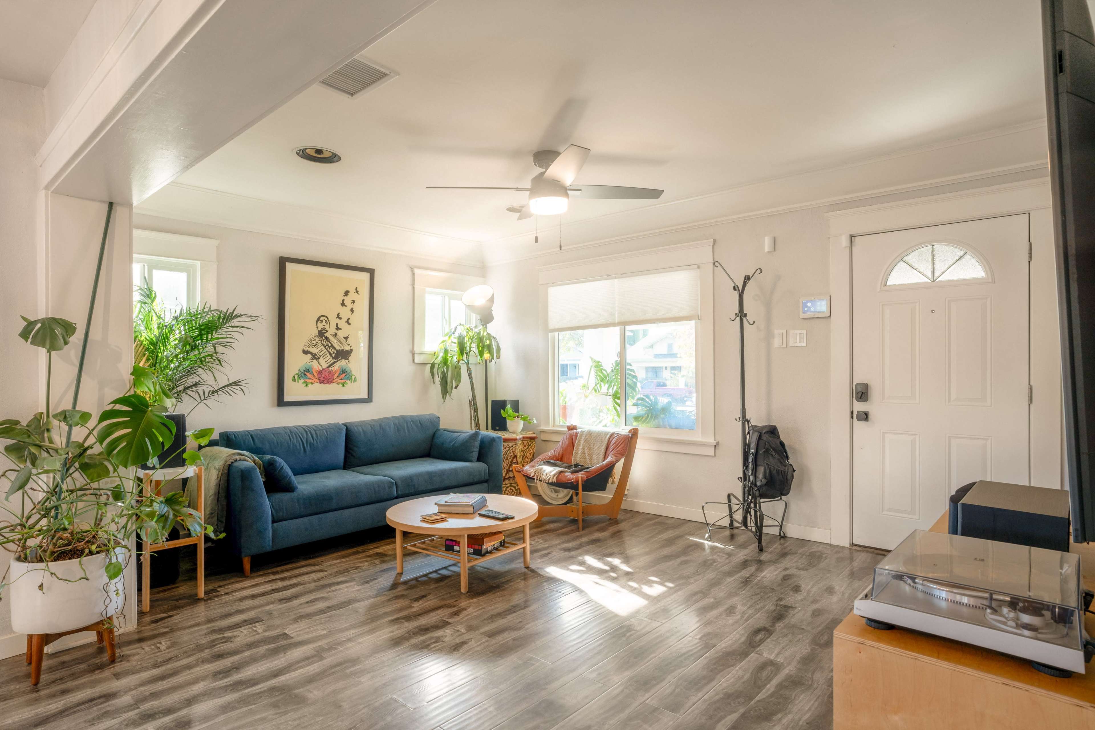 The living room features a blue couch, a round wooden coffee table, and large windows illuminating the space with natural light.
