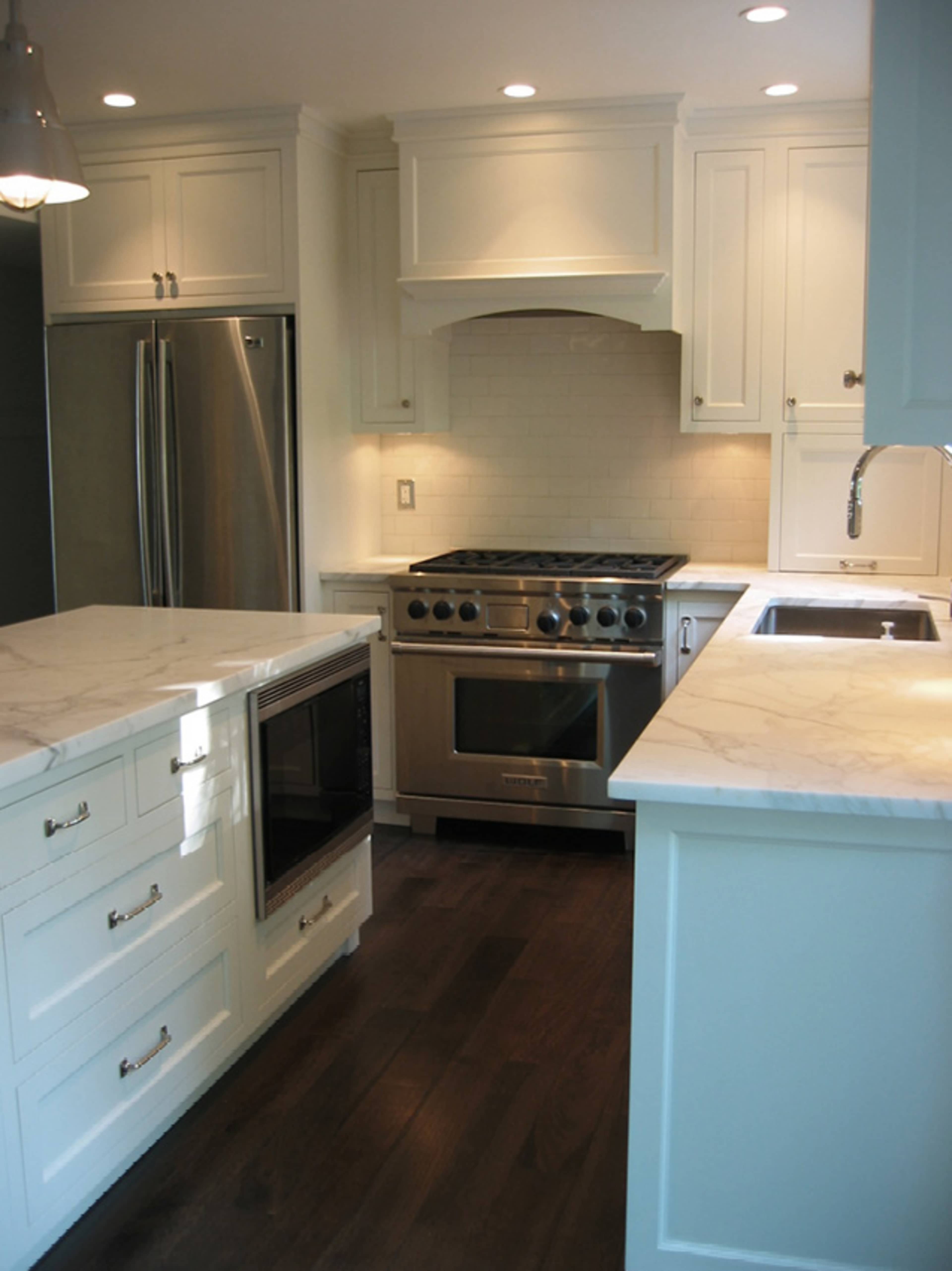 A modern kitchen featuring white cabinetry, marble countertops, and stainless steel appliances.