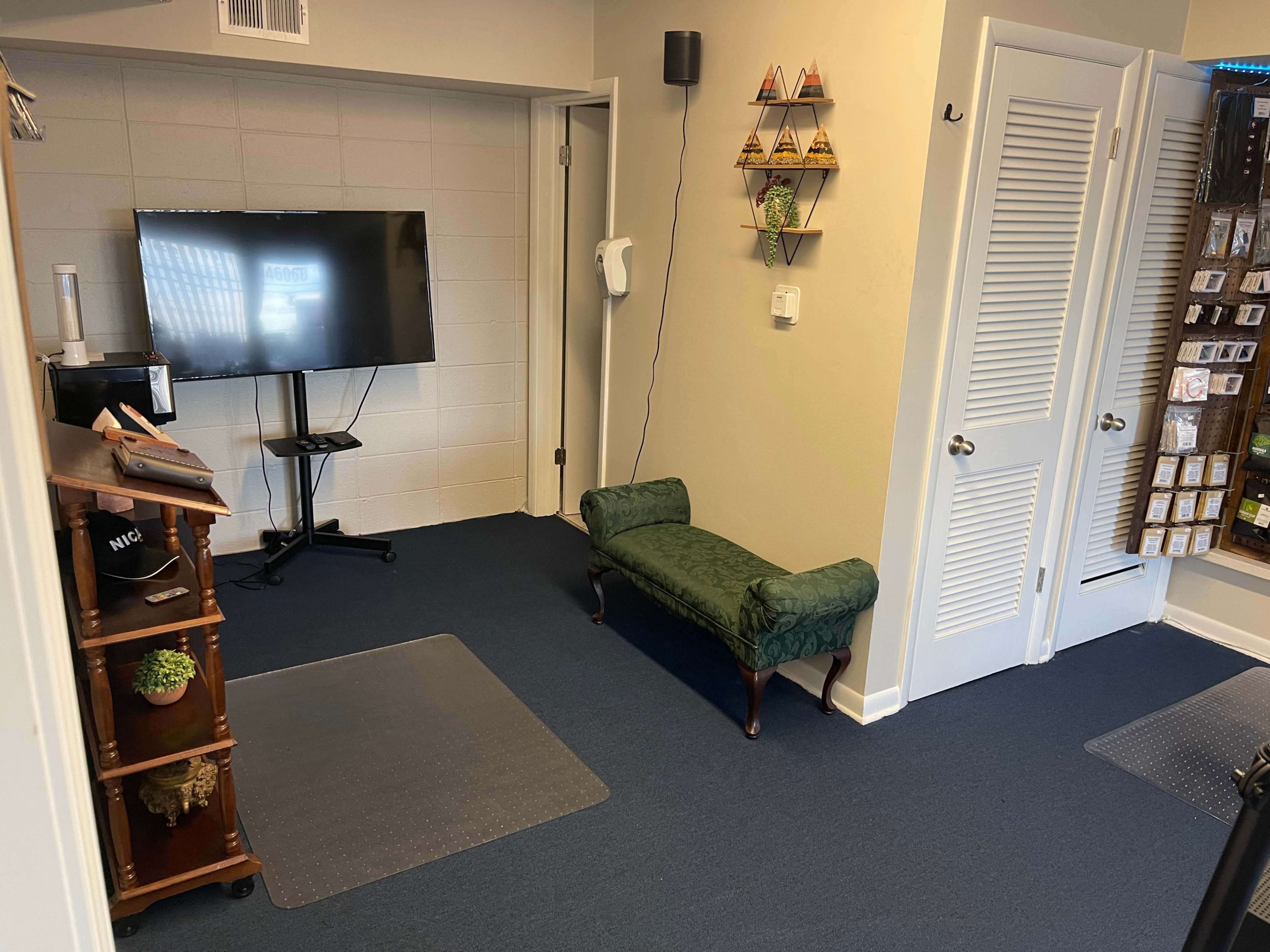 A small room with a television on a stand, a green upholstered bench, and a door leading to another space.