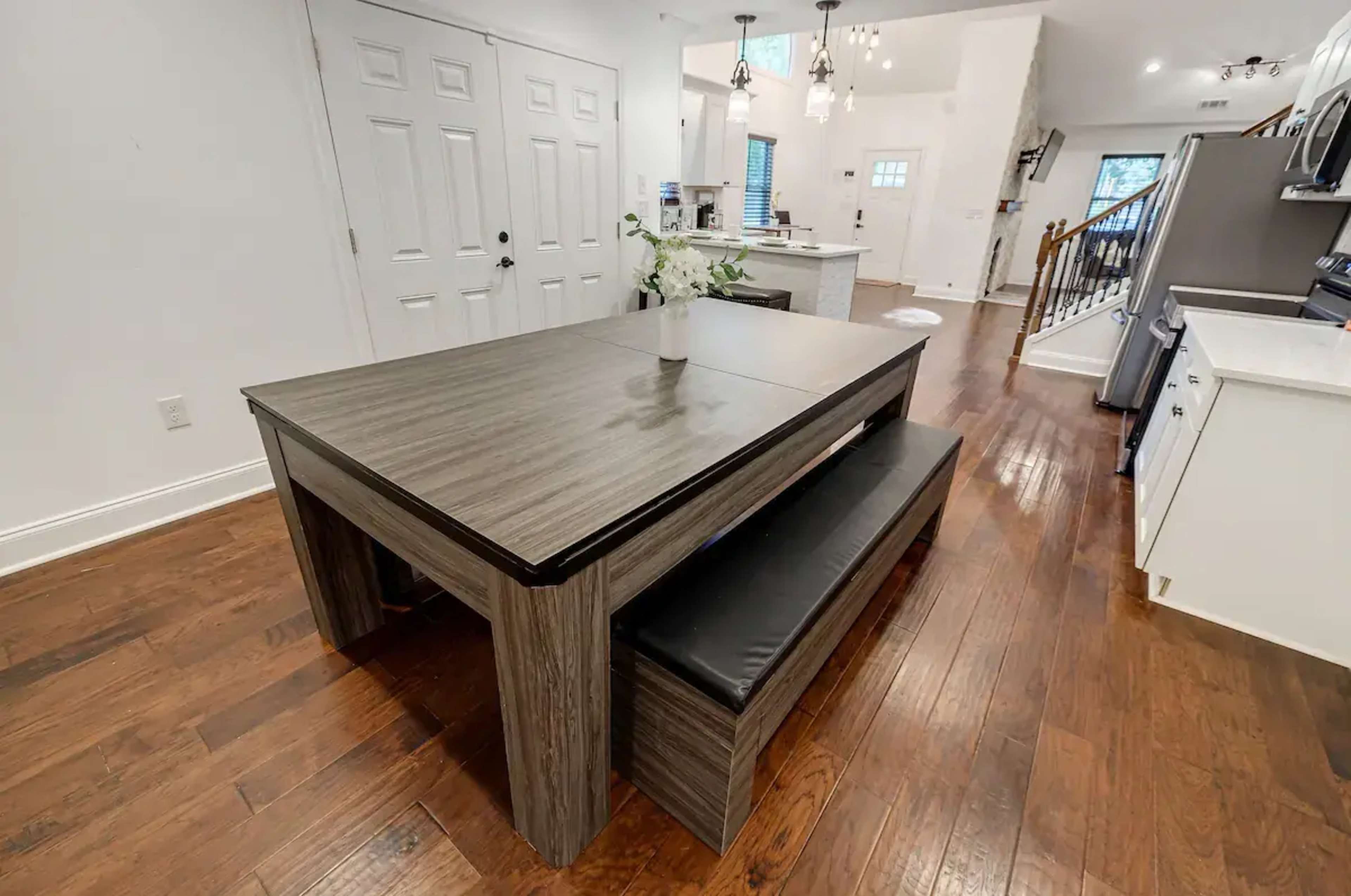 A dining table with a matching bench is positioned in a open kitchen area with white walls and hardwood floors.