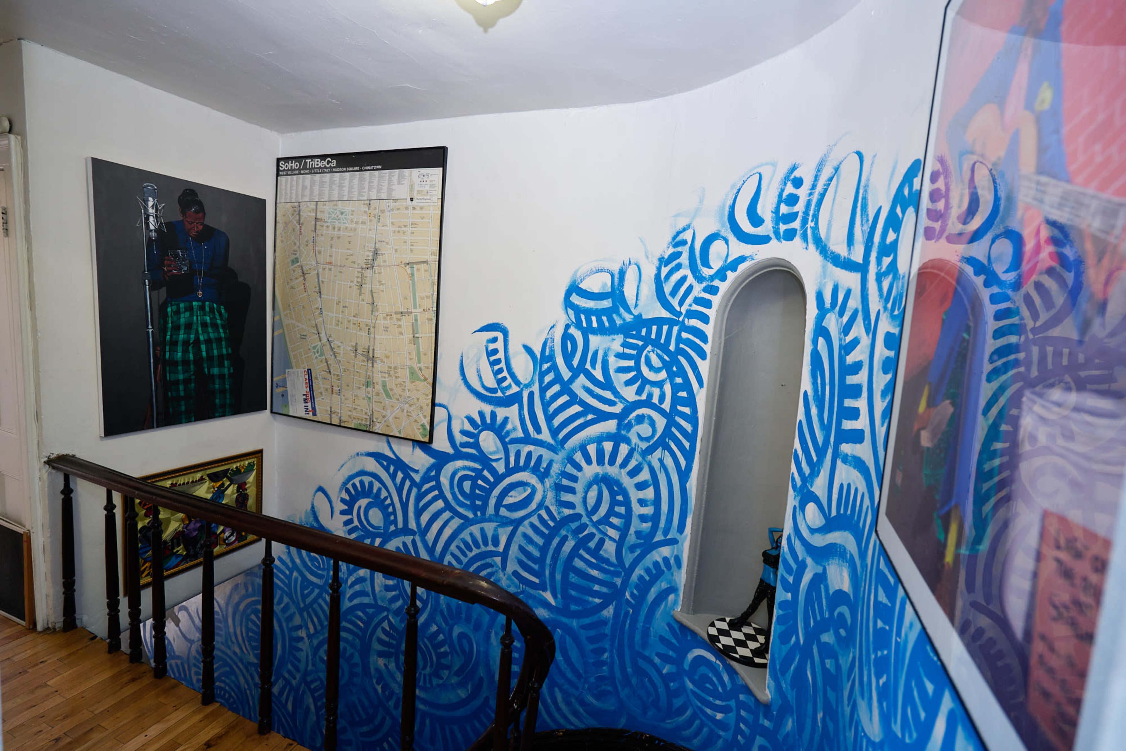 The image shows a staircase with blue abstract wall art, framed pictures on the walls, and a map positioned near a window.
