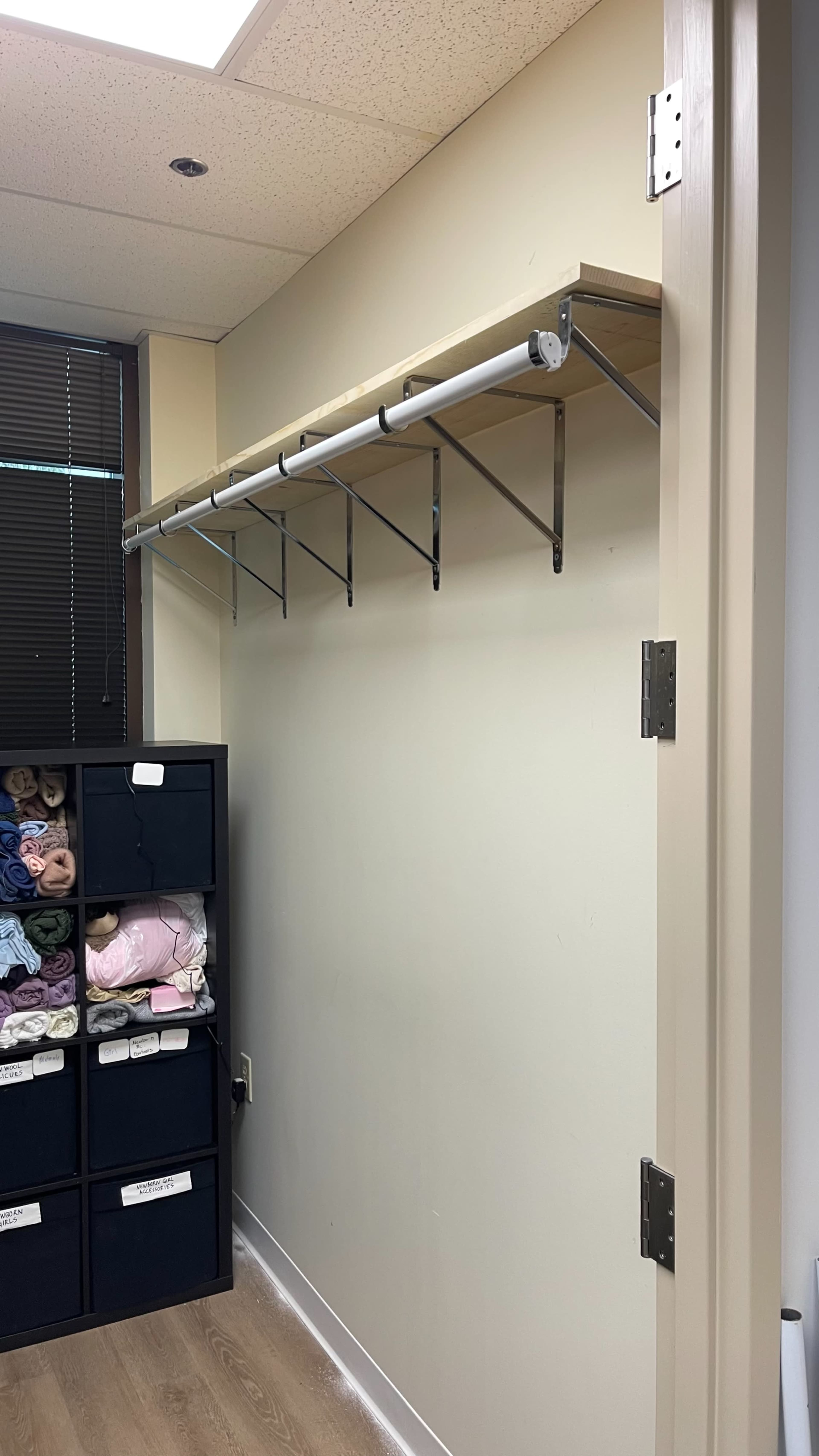 A metal shelf is mounted on the wall above a storage unit containing folded blankets and towels.