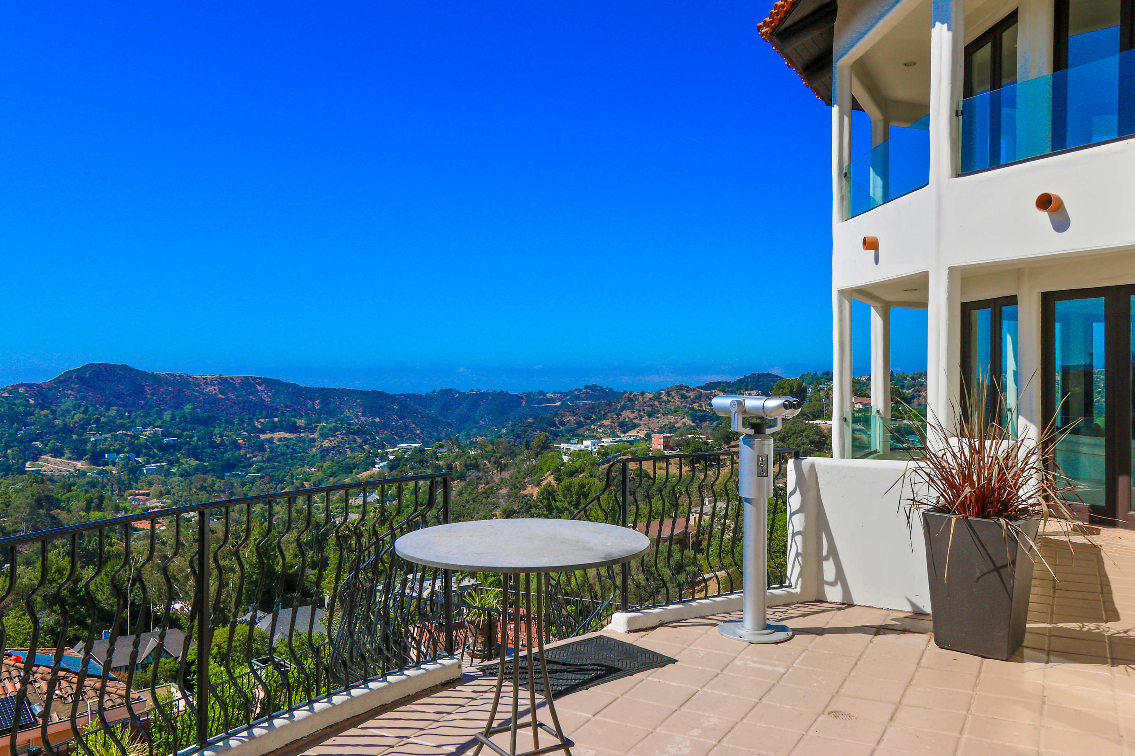 A terrace with a circular table and a view of hills and a clear blue sky in the background.