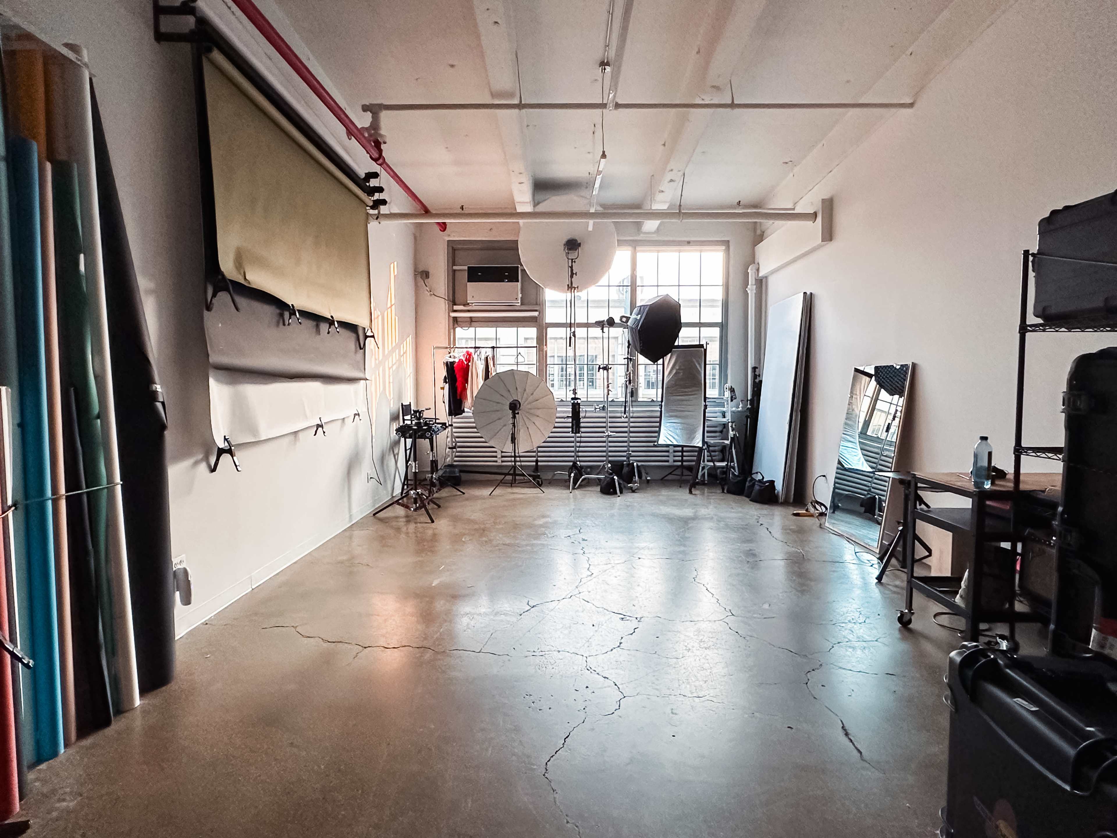 A photography studio with various backdrops, lighting equipment, and a large window allowing natural light.