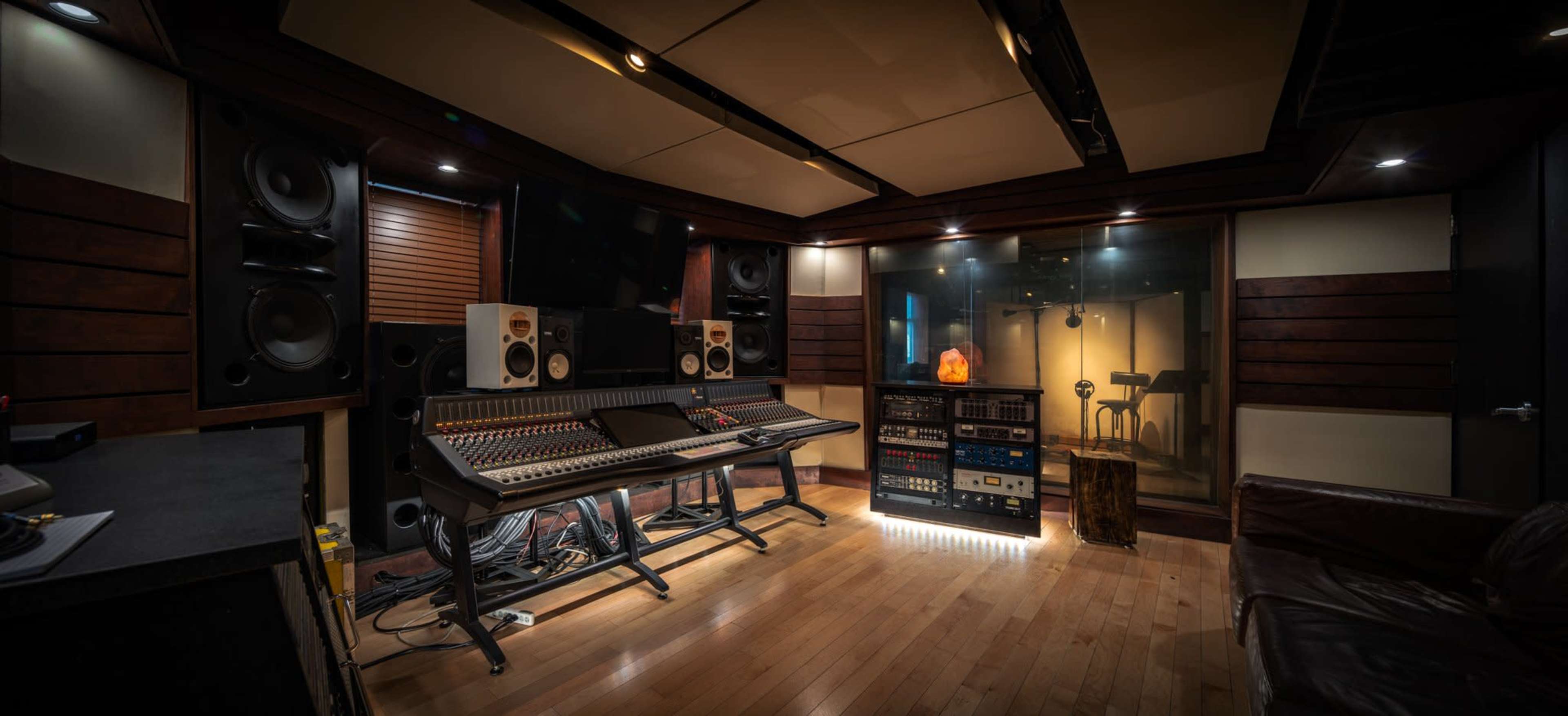 The image shows a recording studio featuring a mixing console, large speakers, and a soundproof glass booth with musical equipment.