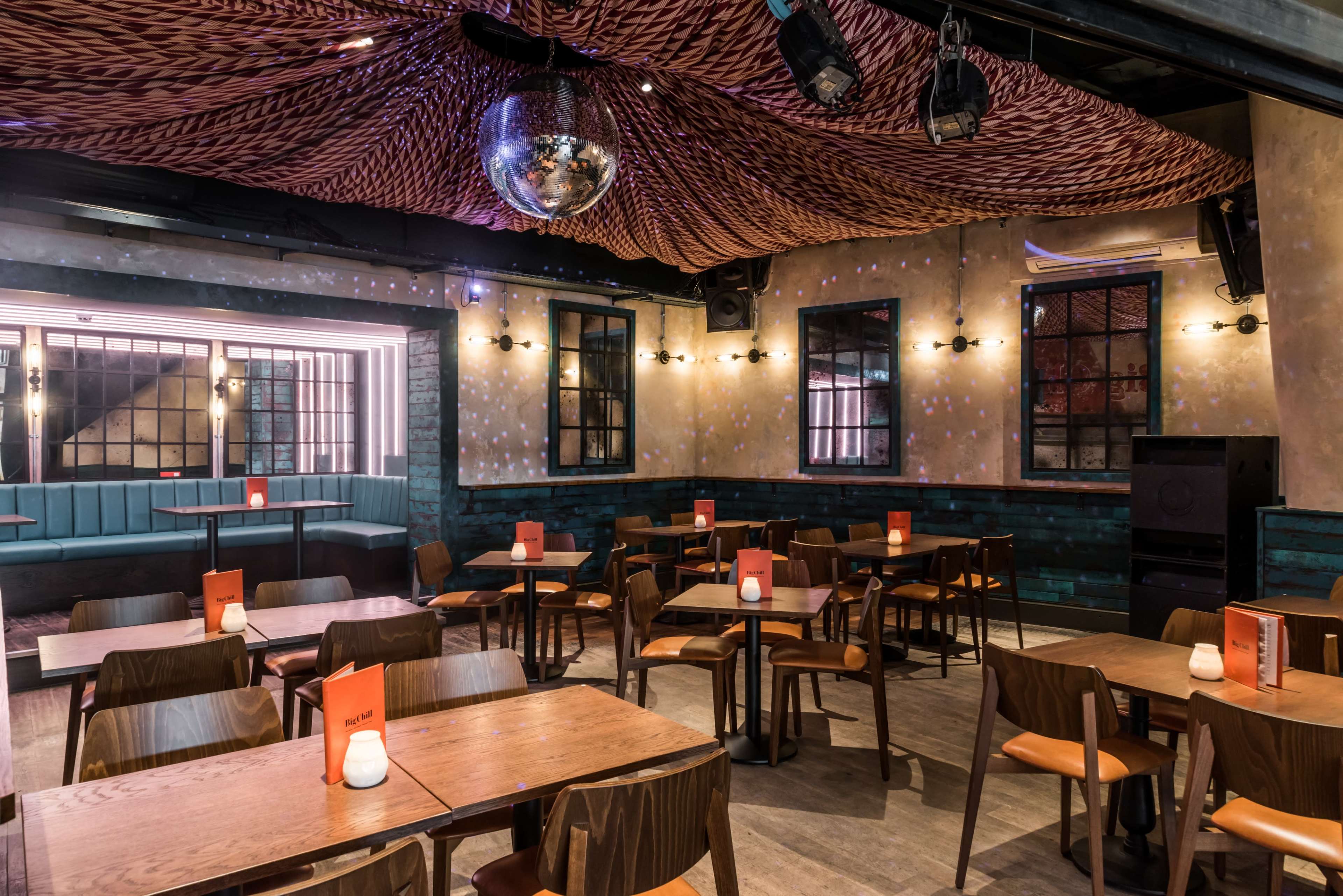 An interior of a restaurant with wooden tables and chairs, featuring a disco ball hanging from the ceiling and illuminated by soft lighting.
