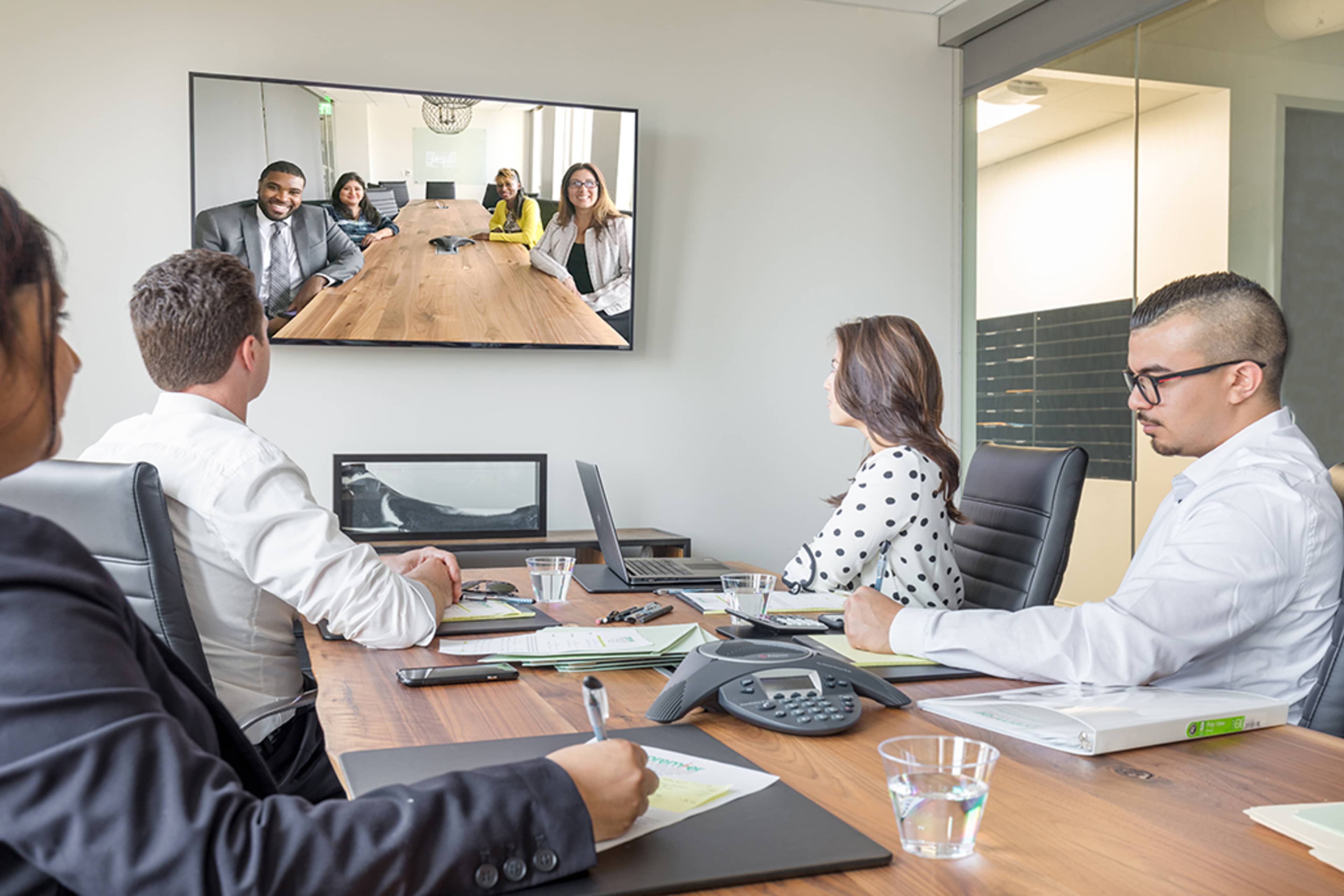 A group of six people participates in a video conference in a modern meeting room.