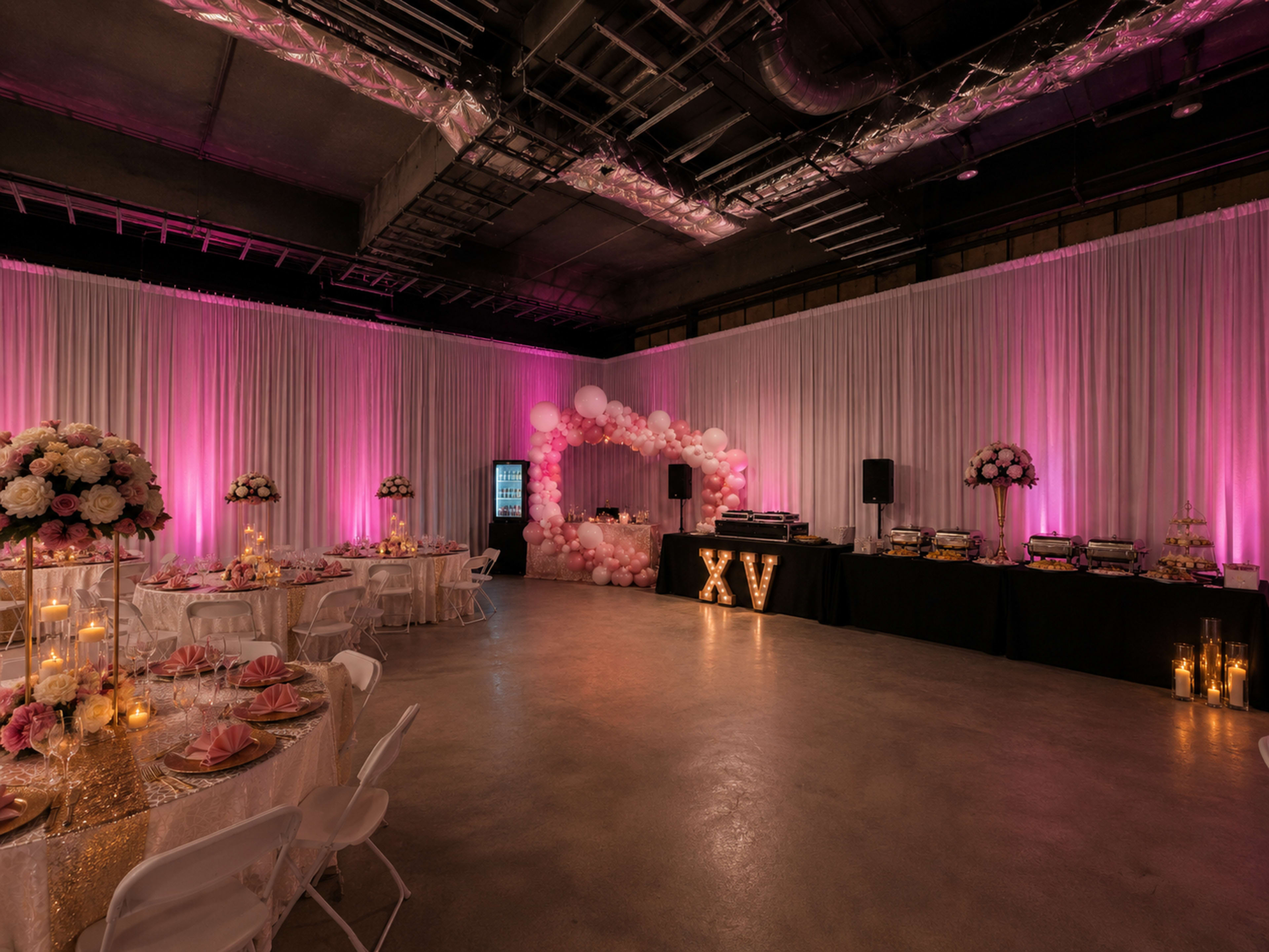 The image shows a decorated event space featuring tables set for a celebration, with pink lighting, floral arrangements, and a prominent "XV" display.