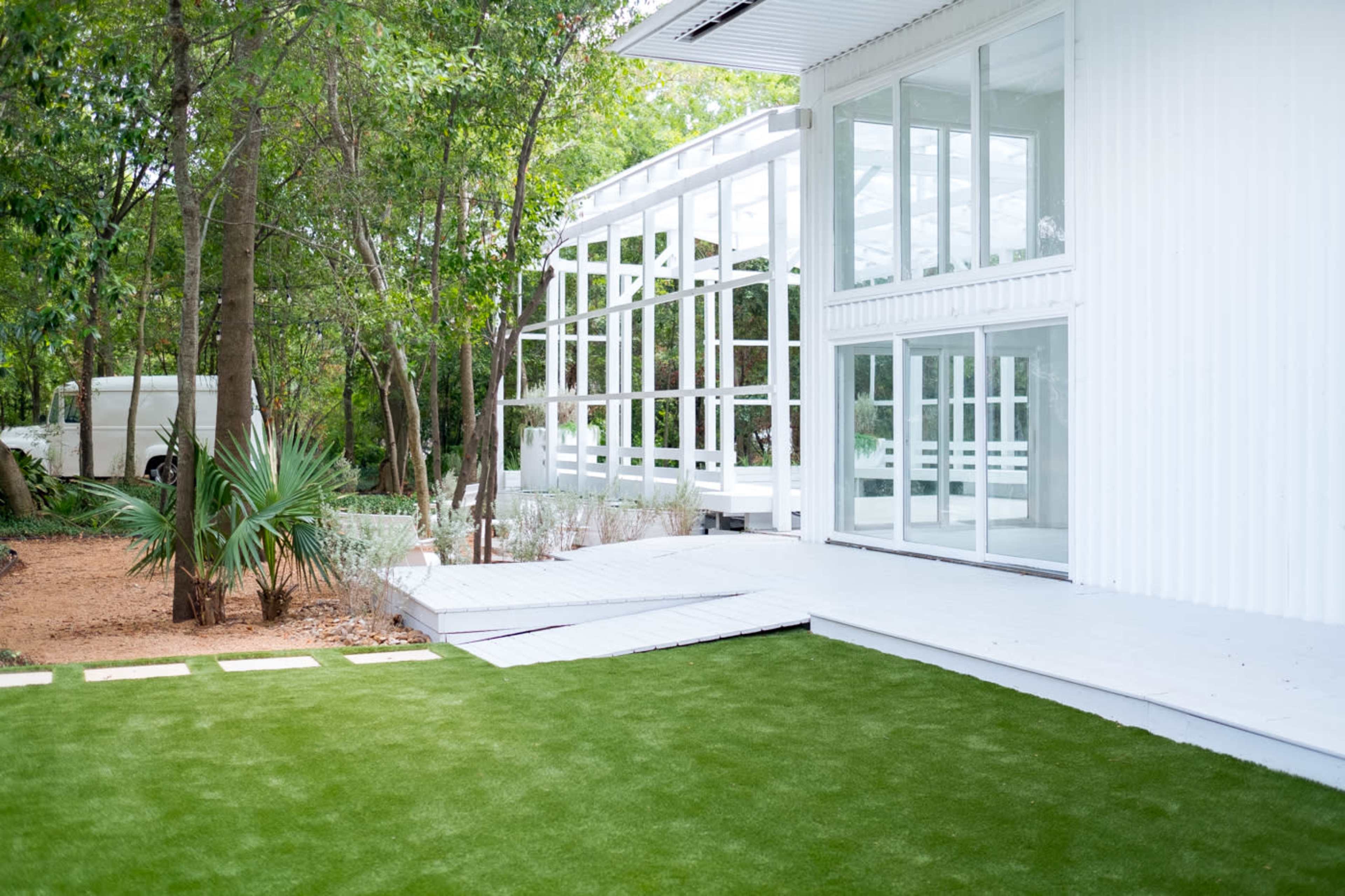 A modern white building with large glass windows, surrounded by green grass and trees.