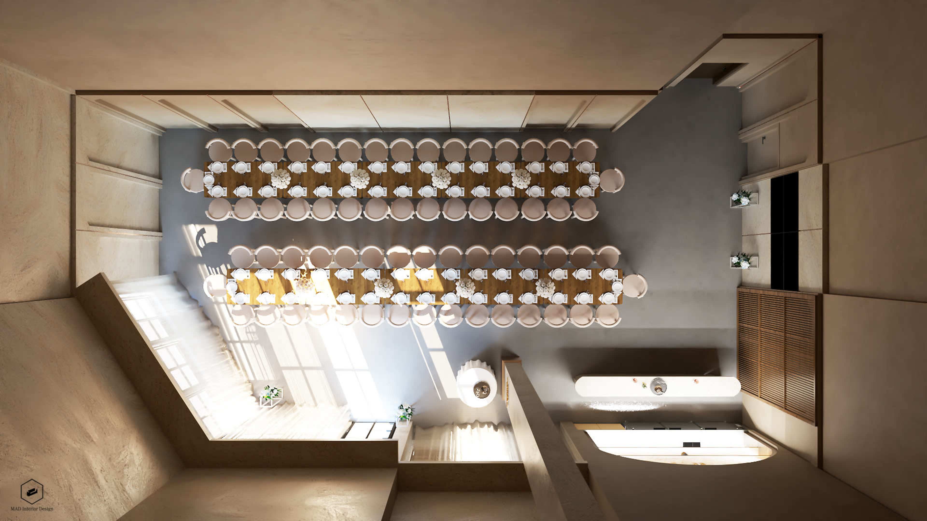 The image shows an overhead view of a spacious dining area arranged with a long table set for an event, surrounded by simple decor and large windows.