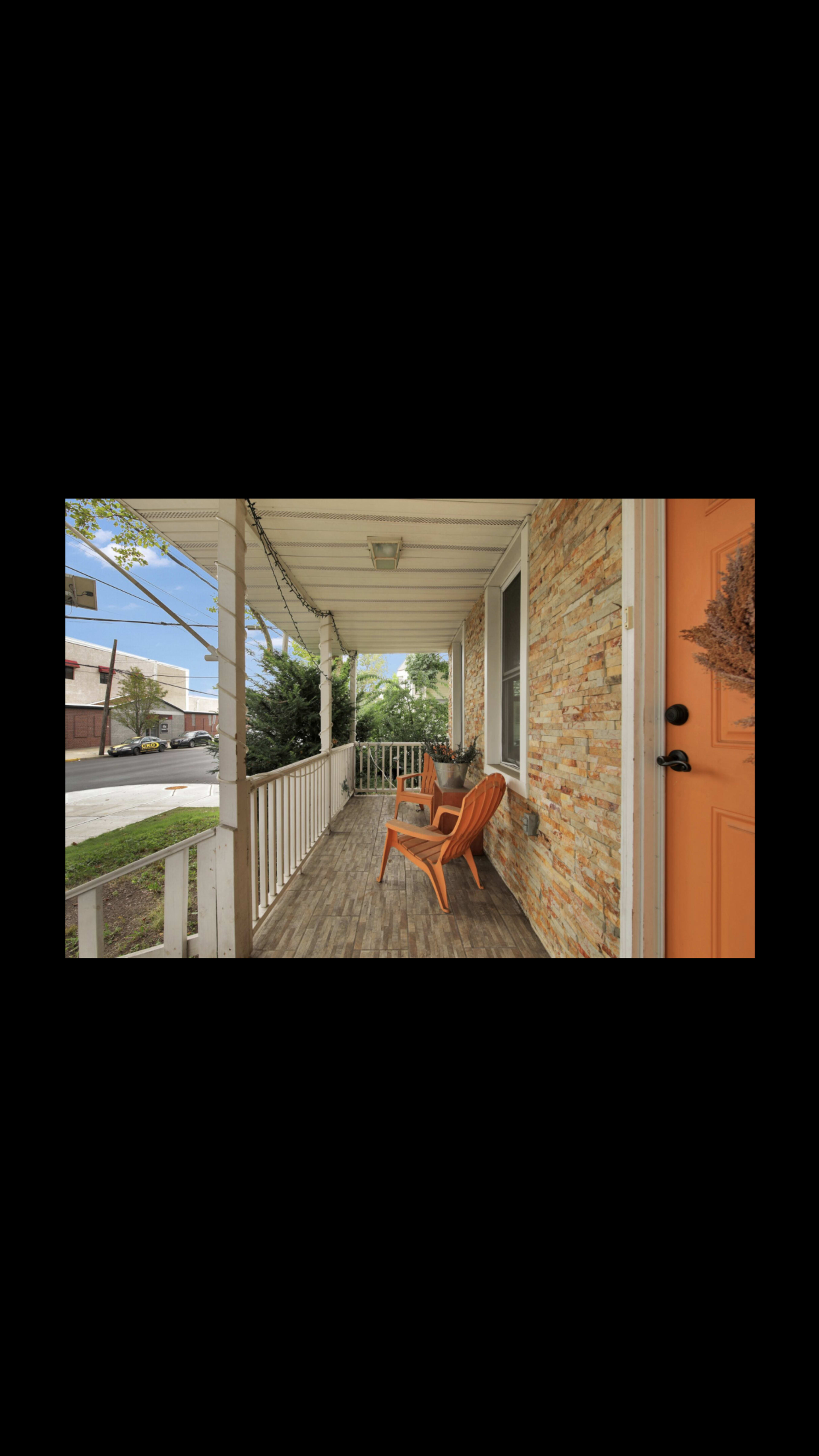 The image shows a porch with two orange chairs, a stone wall, and a vibrant orange door.