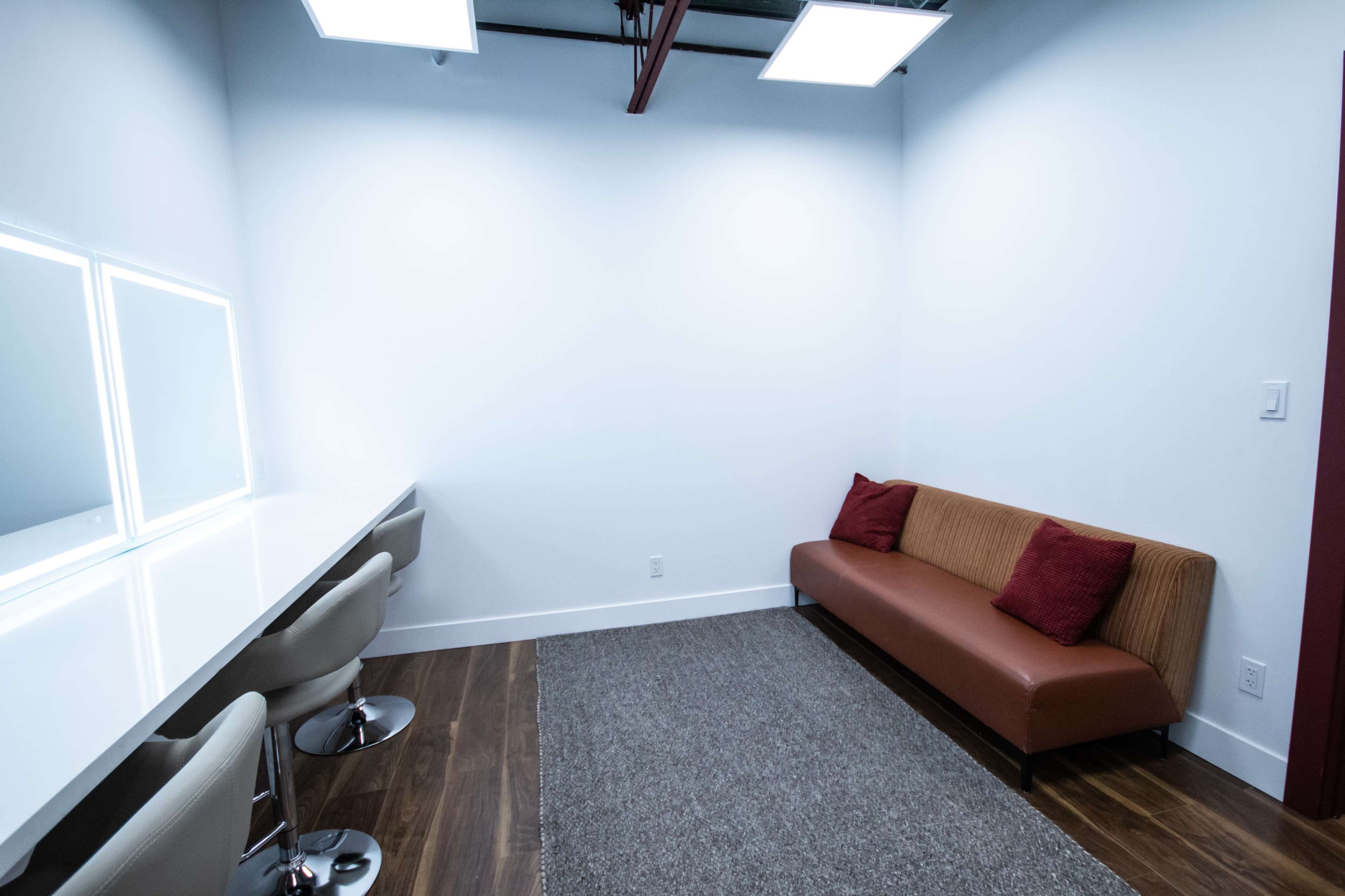 A small room with a brown couch, a long white table with two mirrors, and four modern stools on a wooden floor.