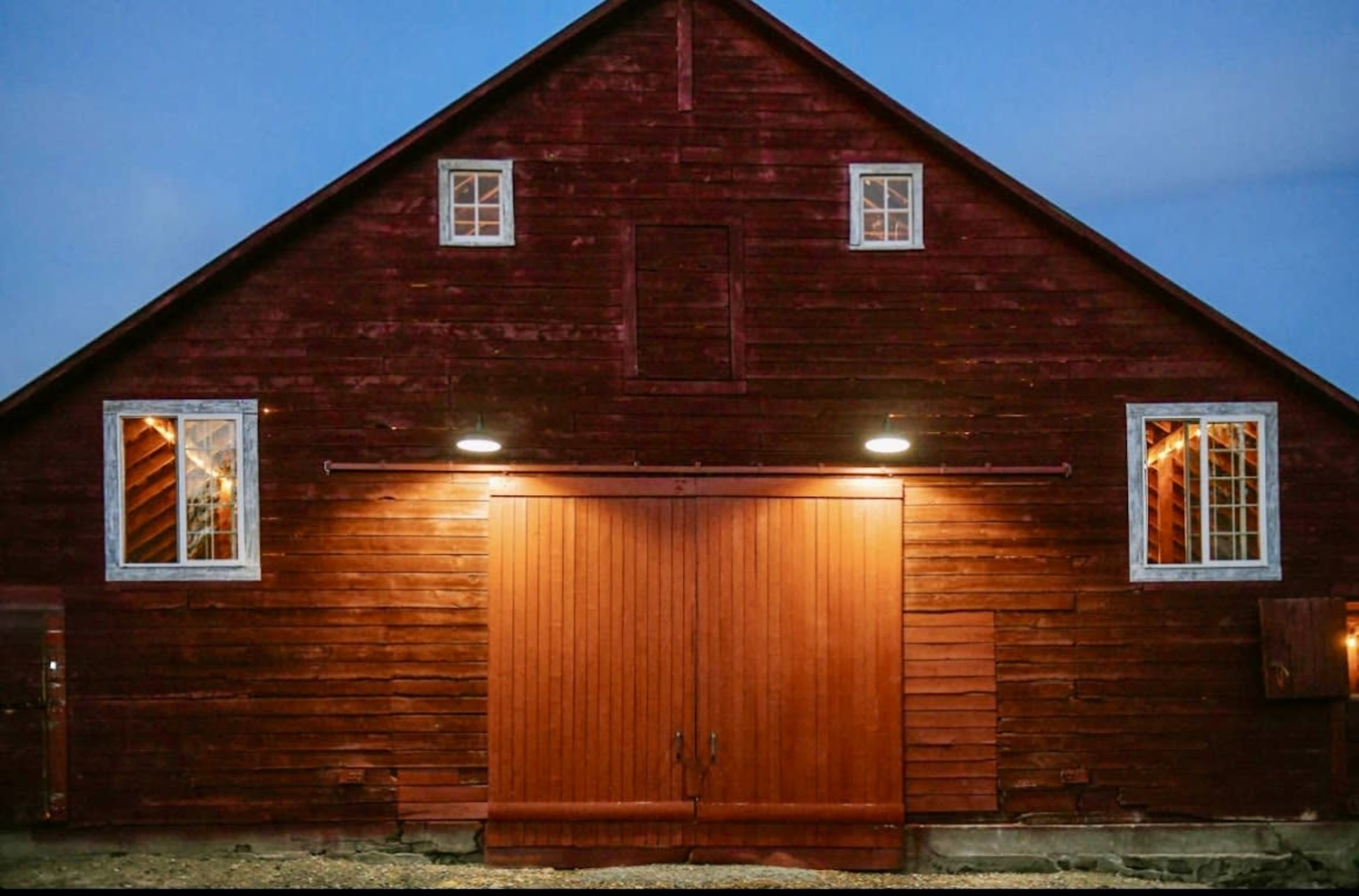 A red barn with wooden double doors is illuminated under the evening sky.