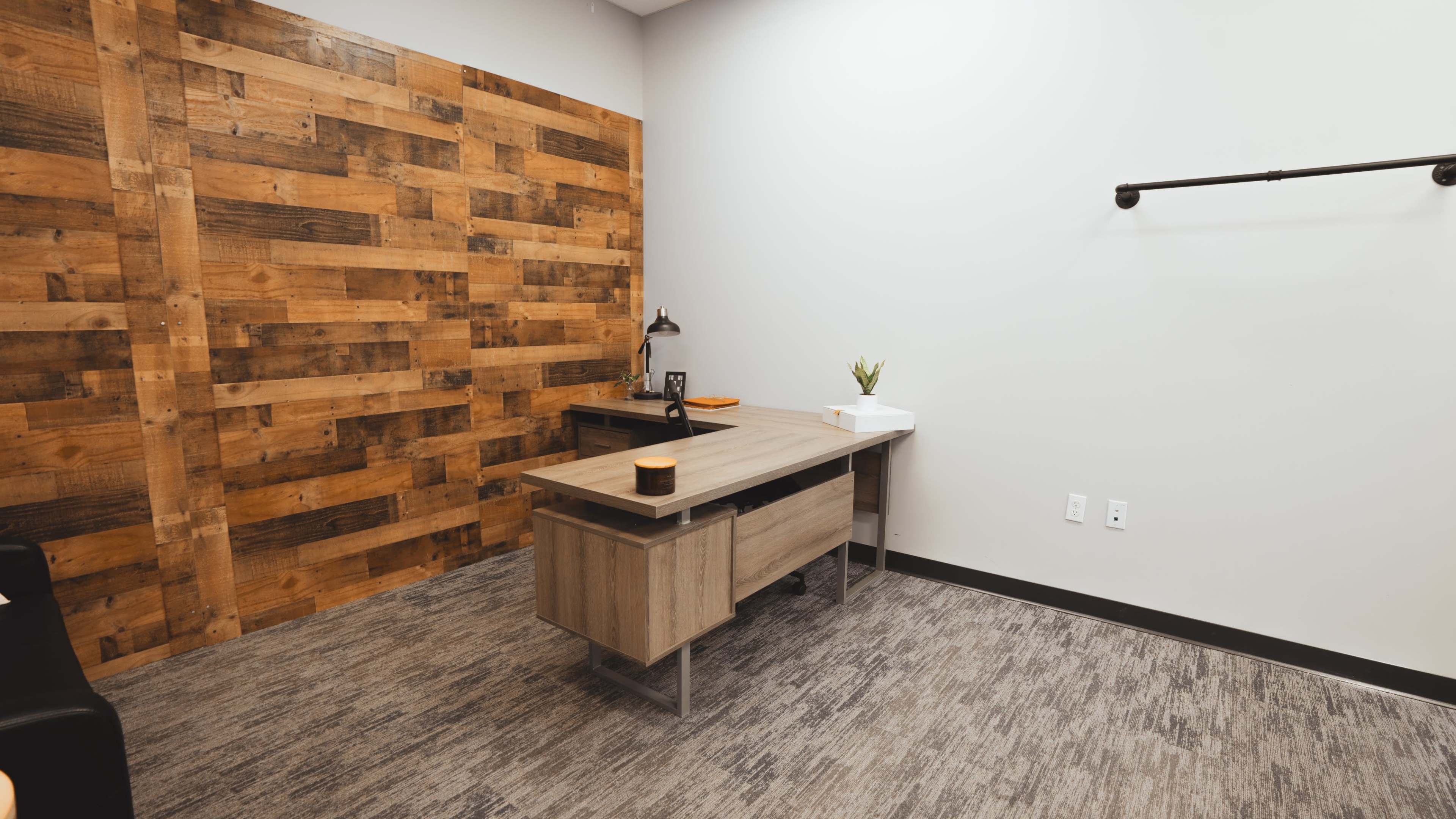 A minimalist office space featuring a wooden accent wall, a desk with a lamp, and a small plant on a shelf.