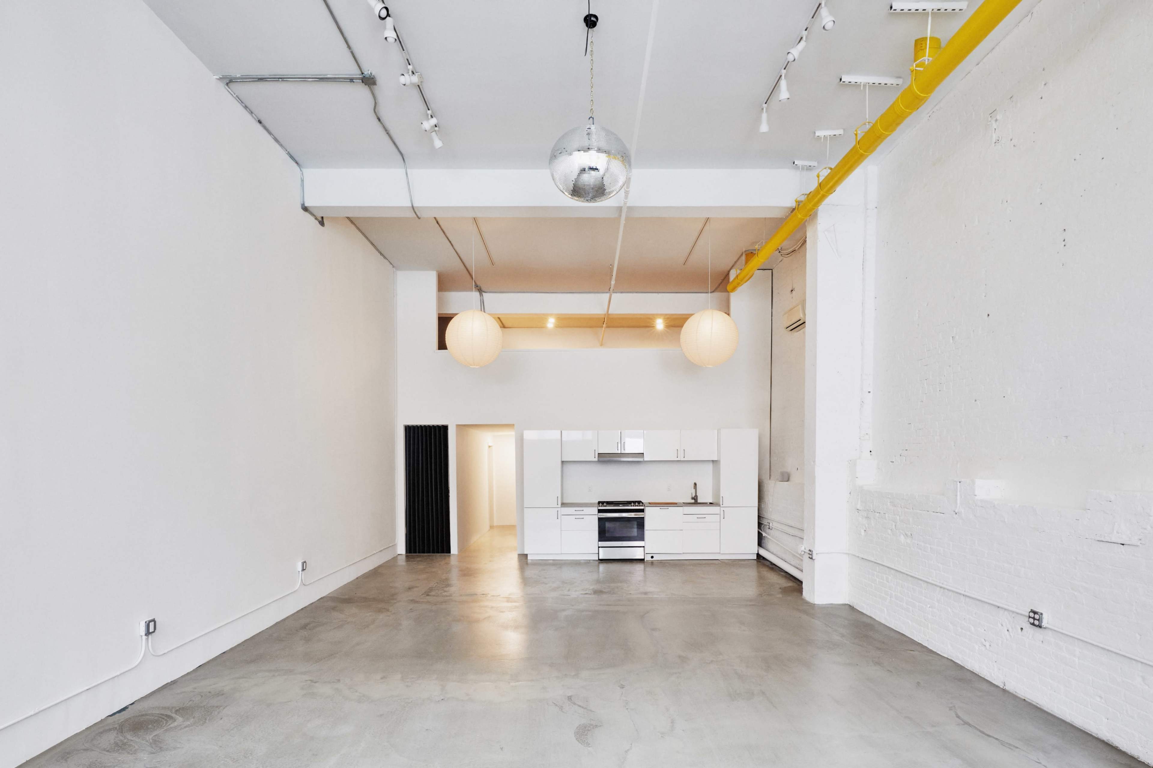 An empty, modern interior space with polished concrete floors, white walls, and a kitchen area in the background.