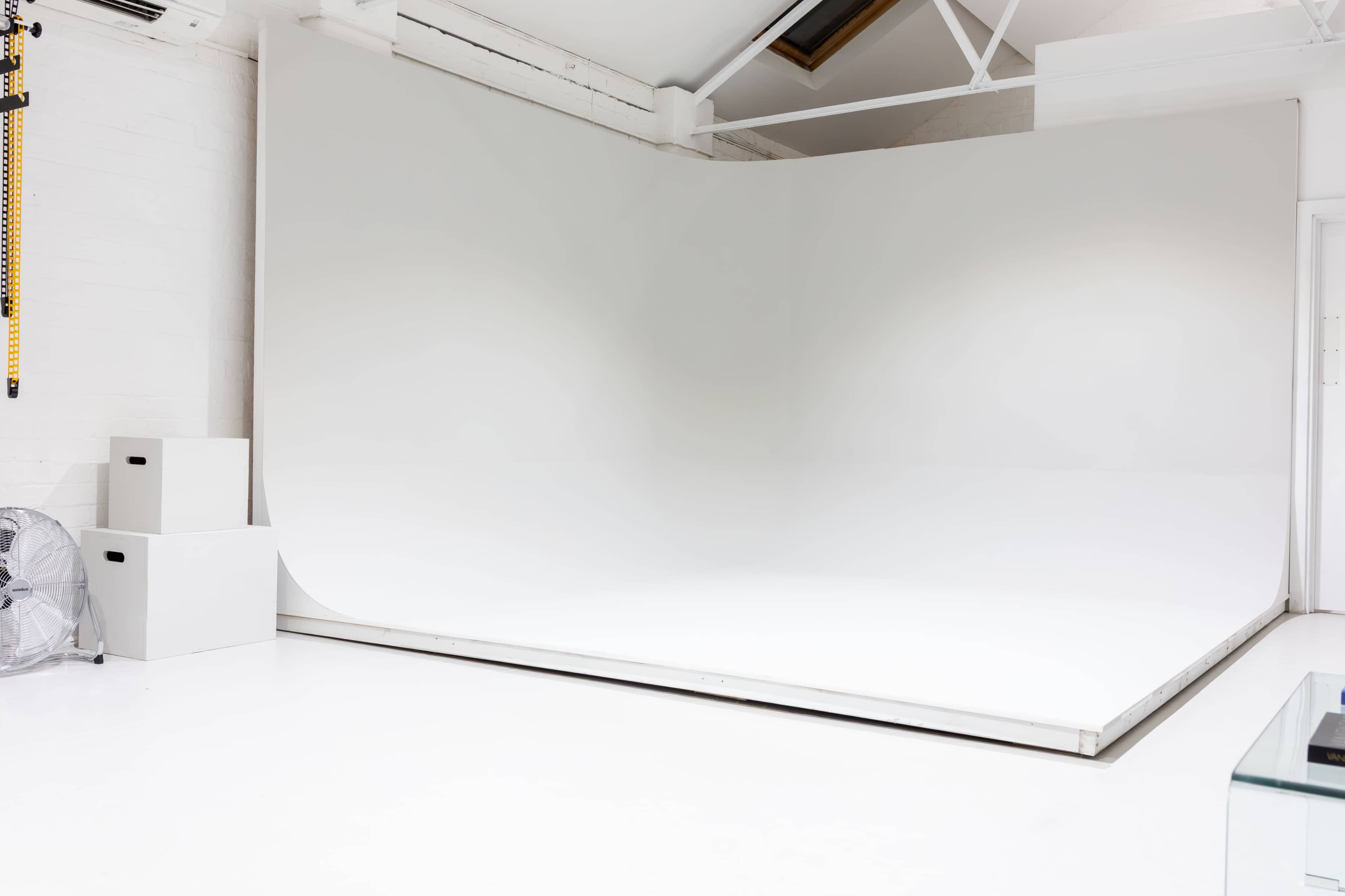 The image shows a spacious photography studio with a seamless white backdrop and minimal furniture.