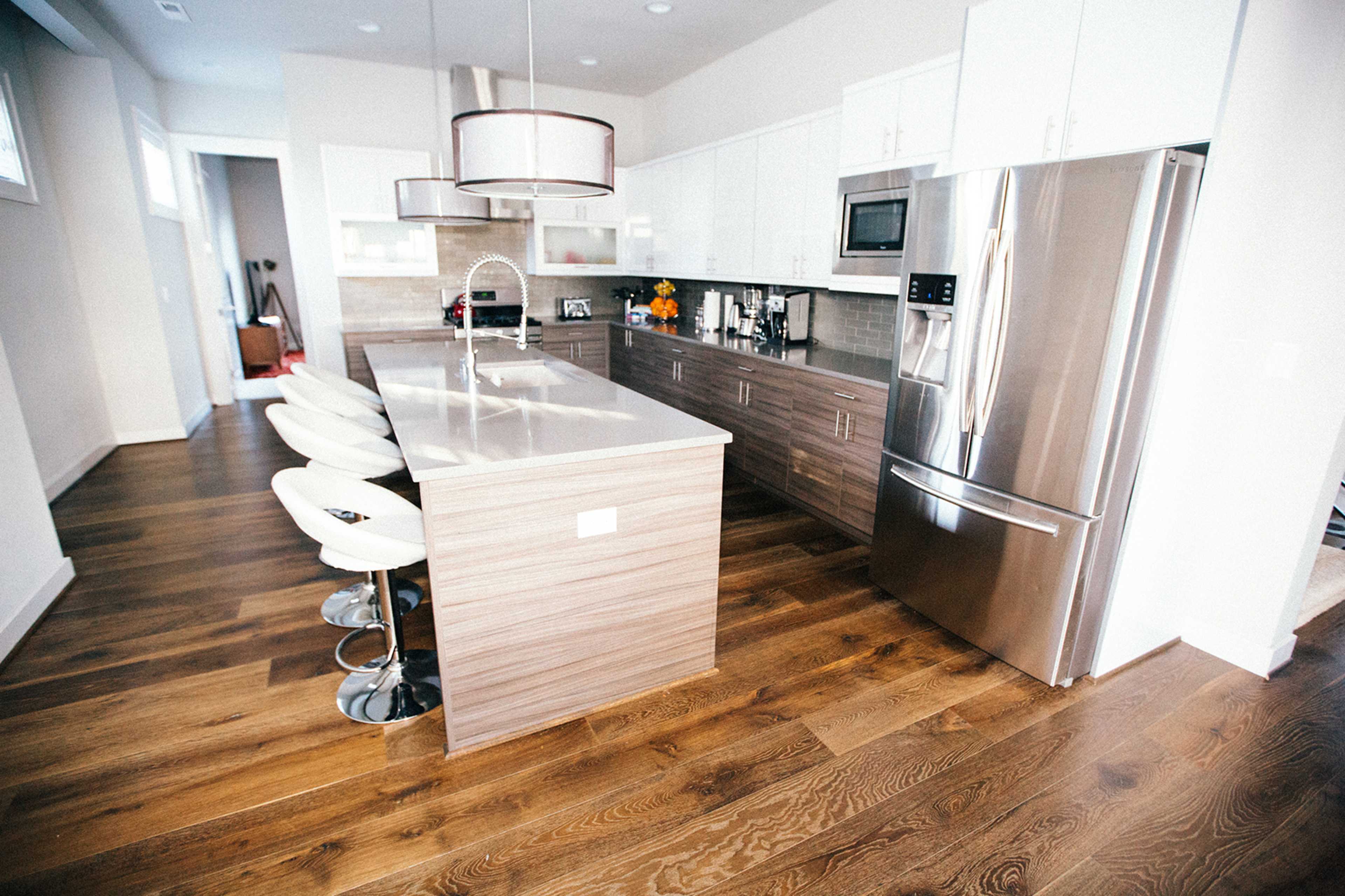 A modern kitchen with a large island featuring bar stools, stainless steel appliances, and light-colored cabinetry.