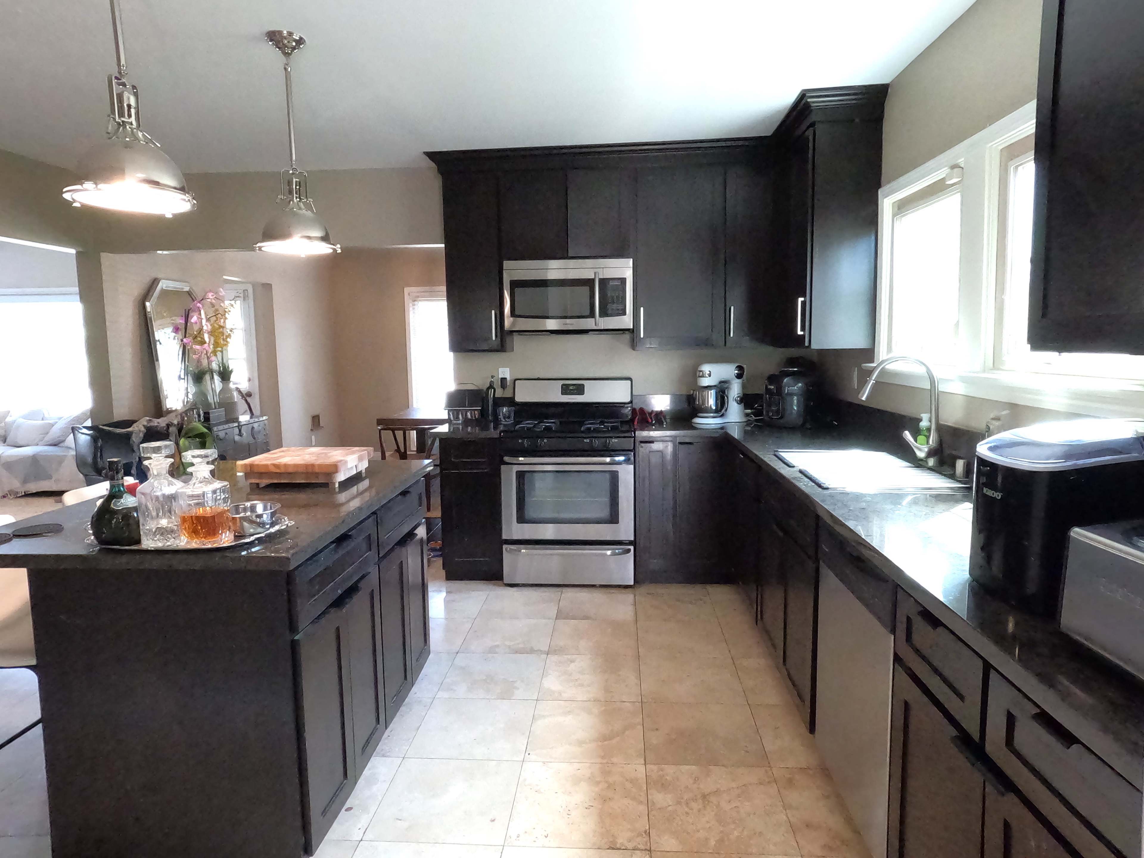 The image shows a modern kitchen with dark cabinetry, stainless steel appliances, and a granite countertop.
