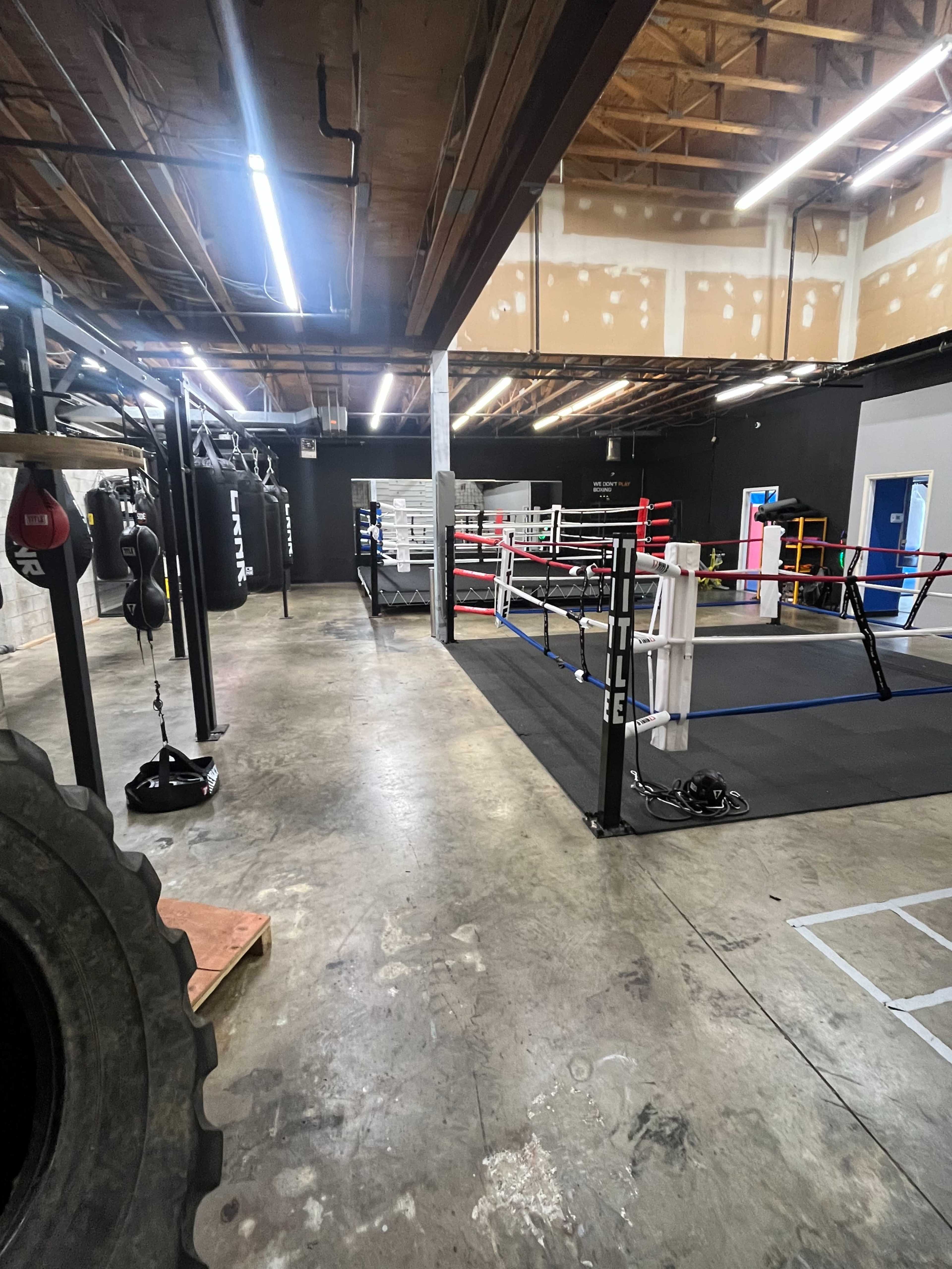 The image shows a boxing gym with several training stations, including a ring, punching bags, and open floor space.
