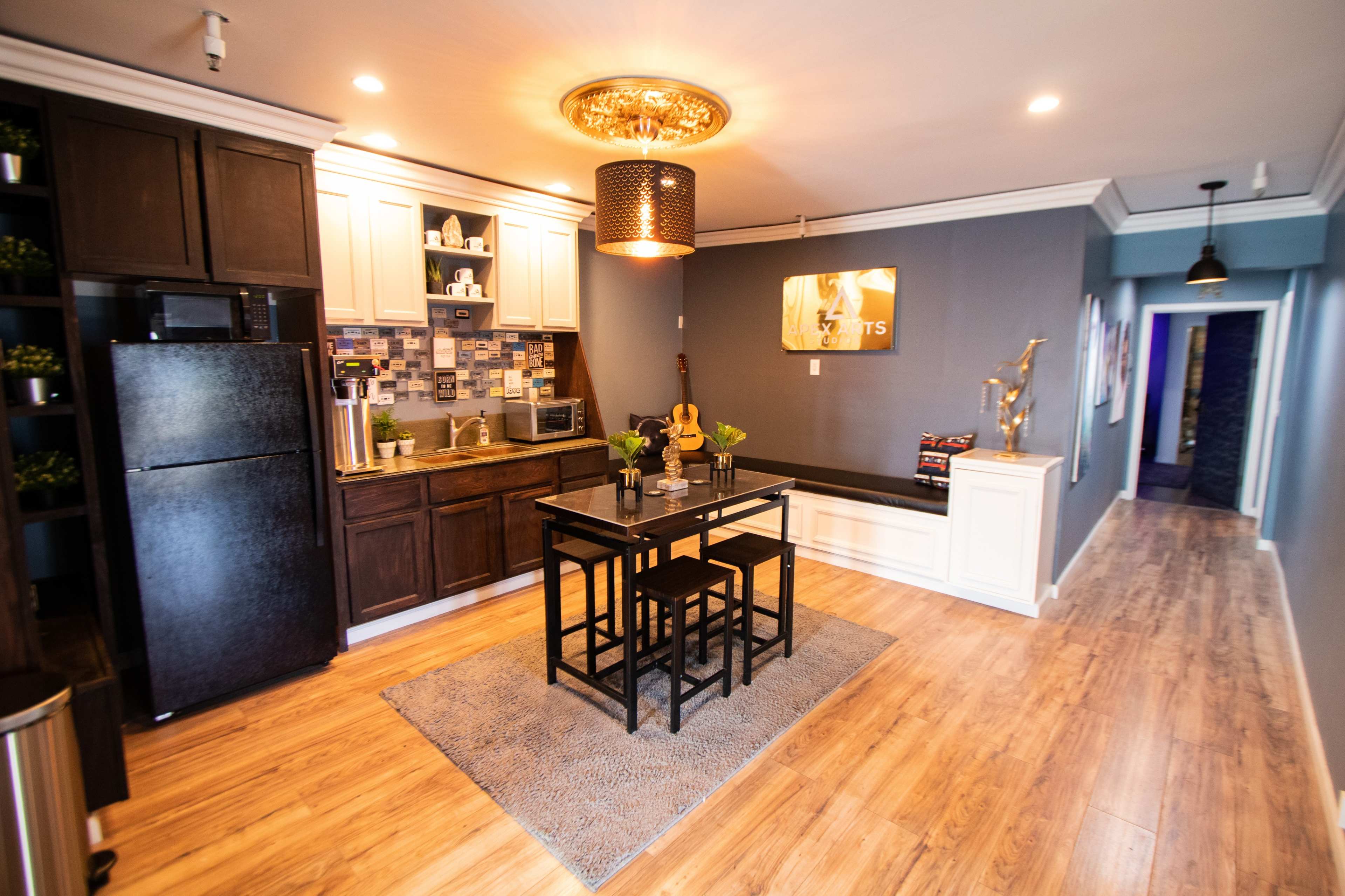 A modern, open-concept kitchen and dining area with dark cabinetry, a black table set for four, and a hallway leading to another room.
