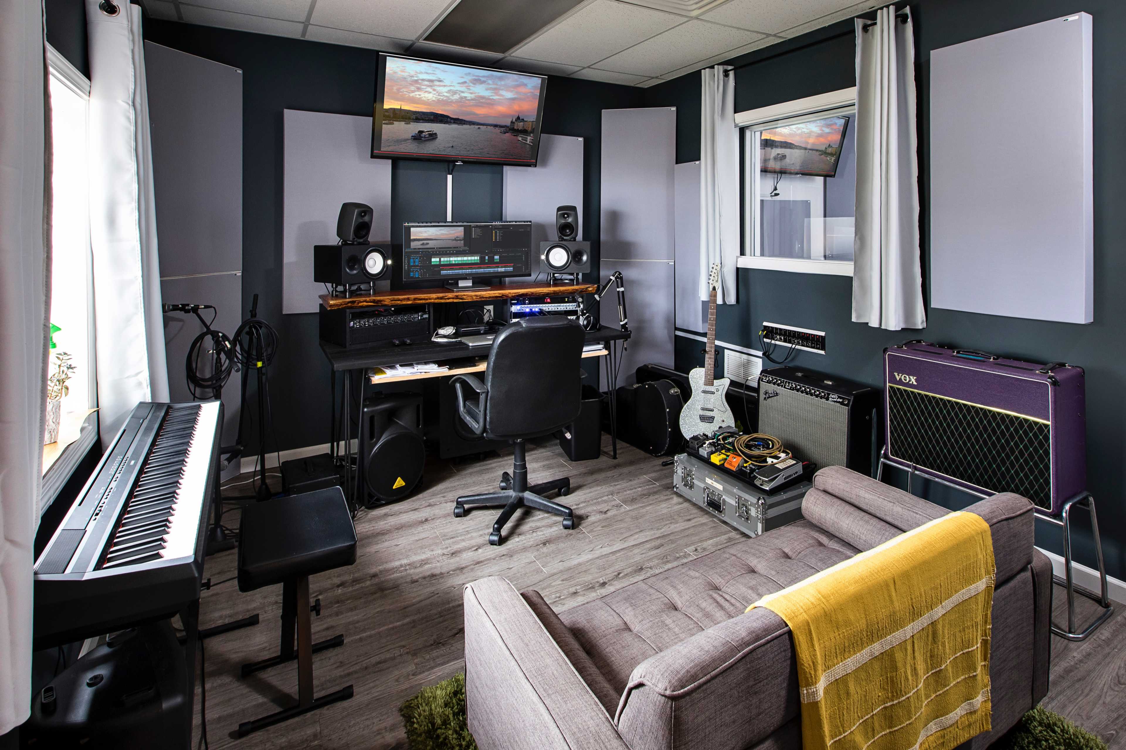 A modern music studio with a keyboard, audio equipment, and seating arranged around a central workspace.