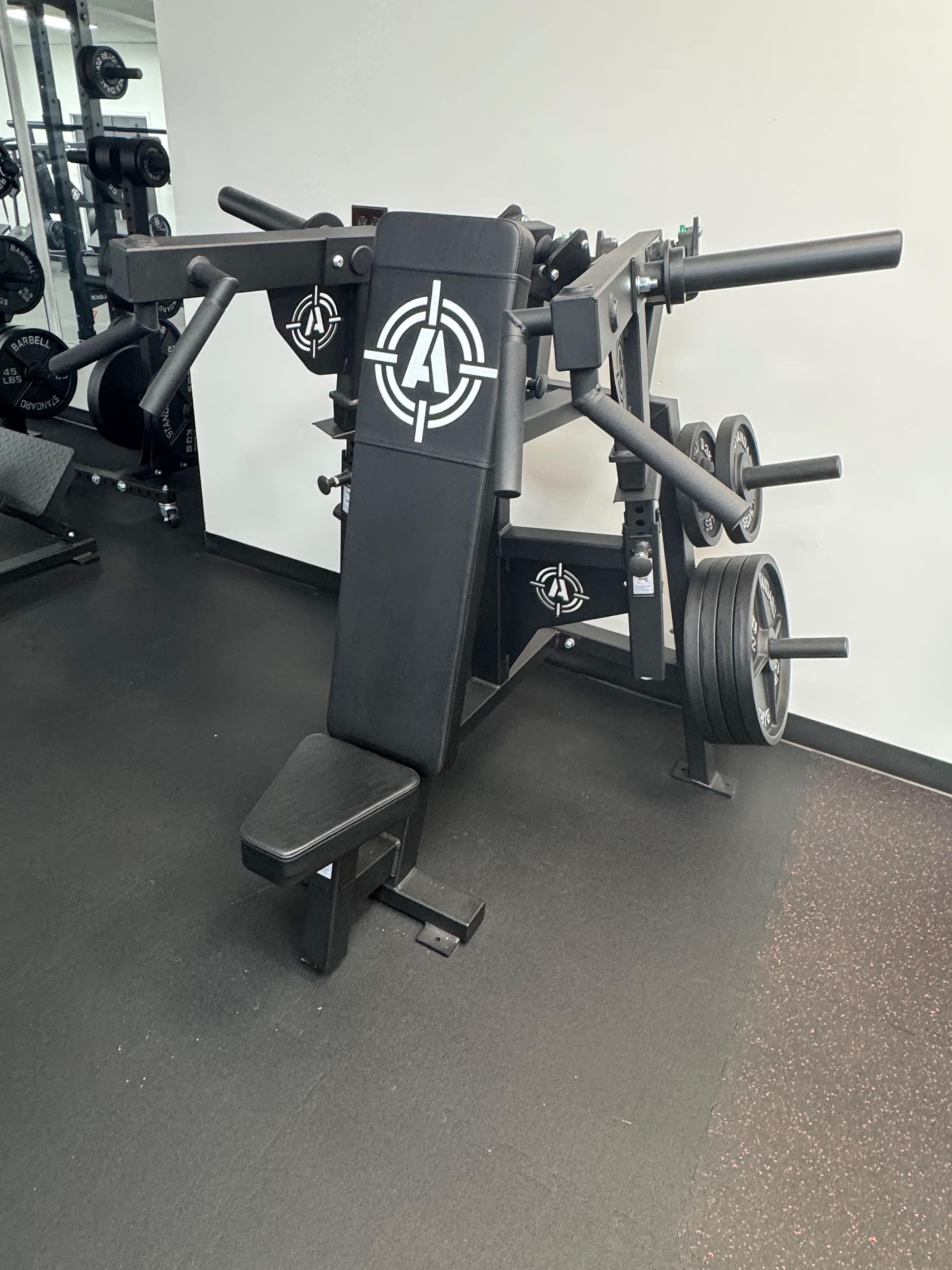 The image shows a multi-functional weightlifting machine with adjustable components and weight plates in a gym setting.