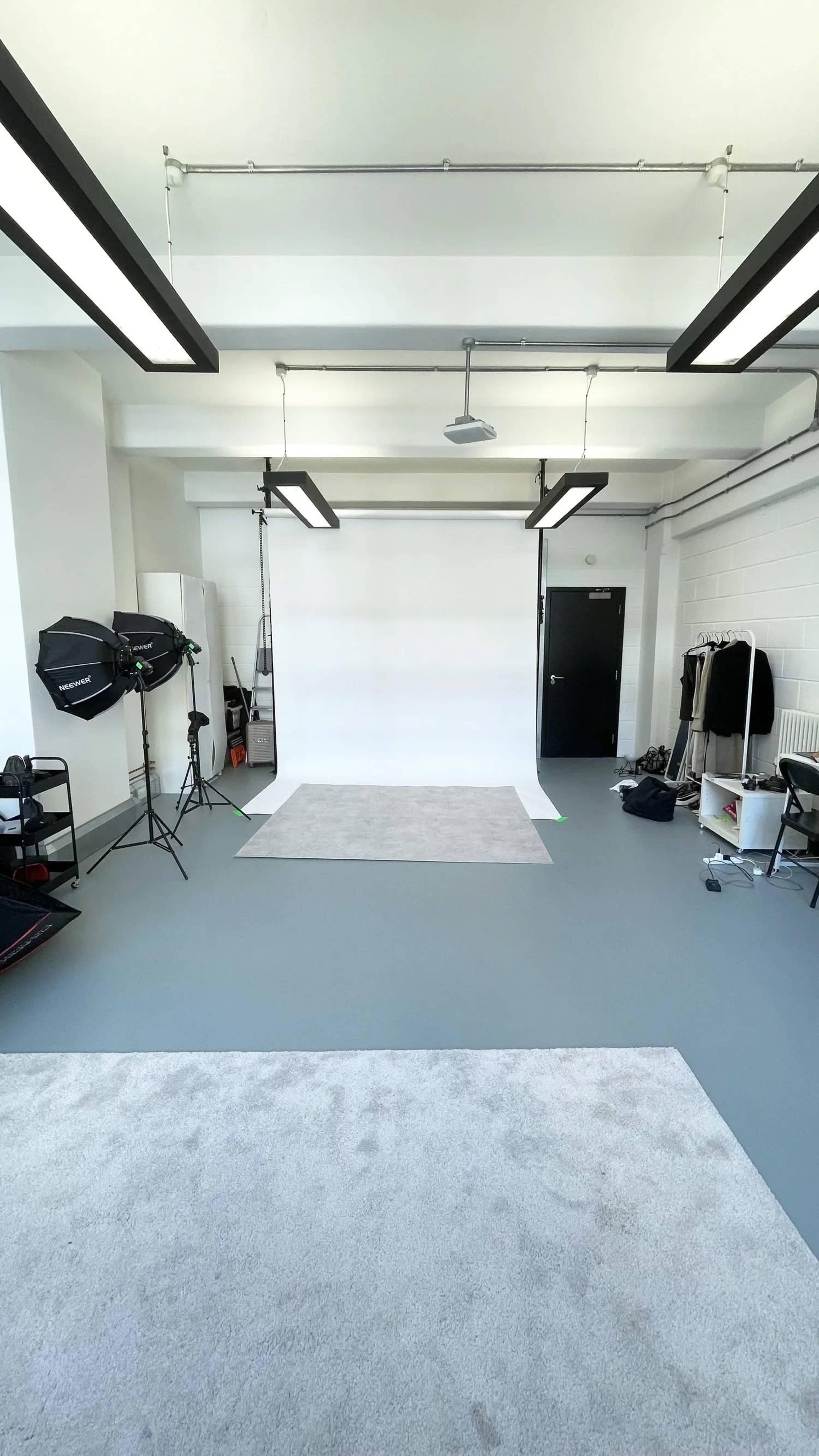 The image shows a bright studio space with a white backdrop, lighting equipment, and various props arranged around the room.