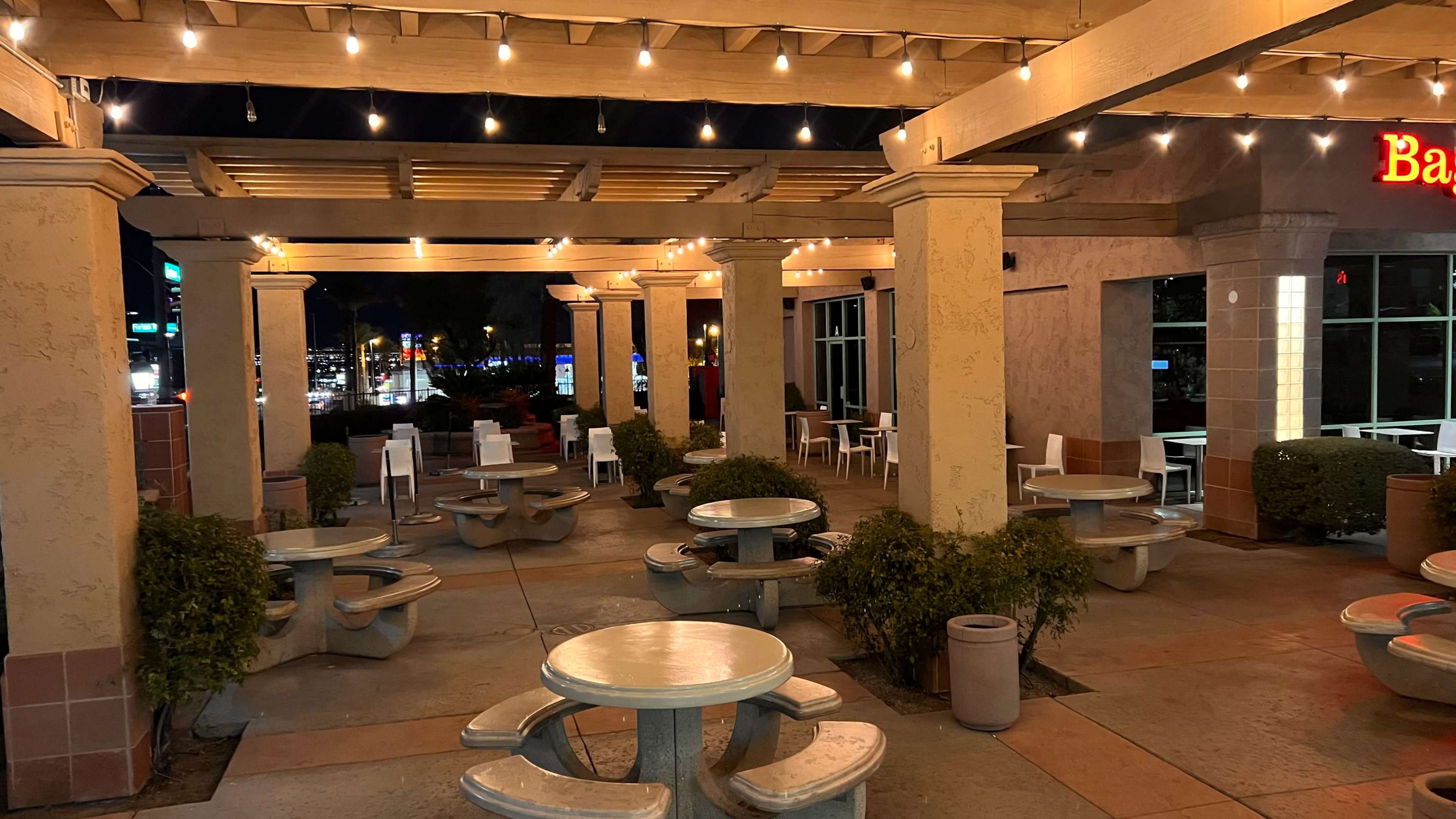 An outdoor dining area at night, complete with circular tables, bench seating, and string lights overhead.