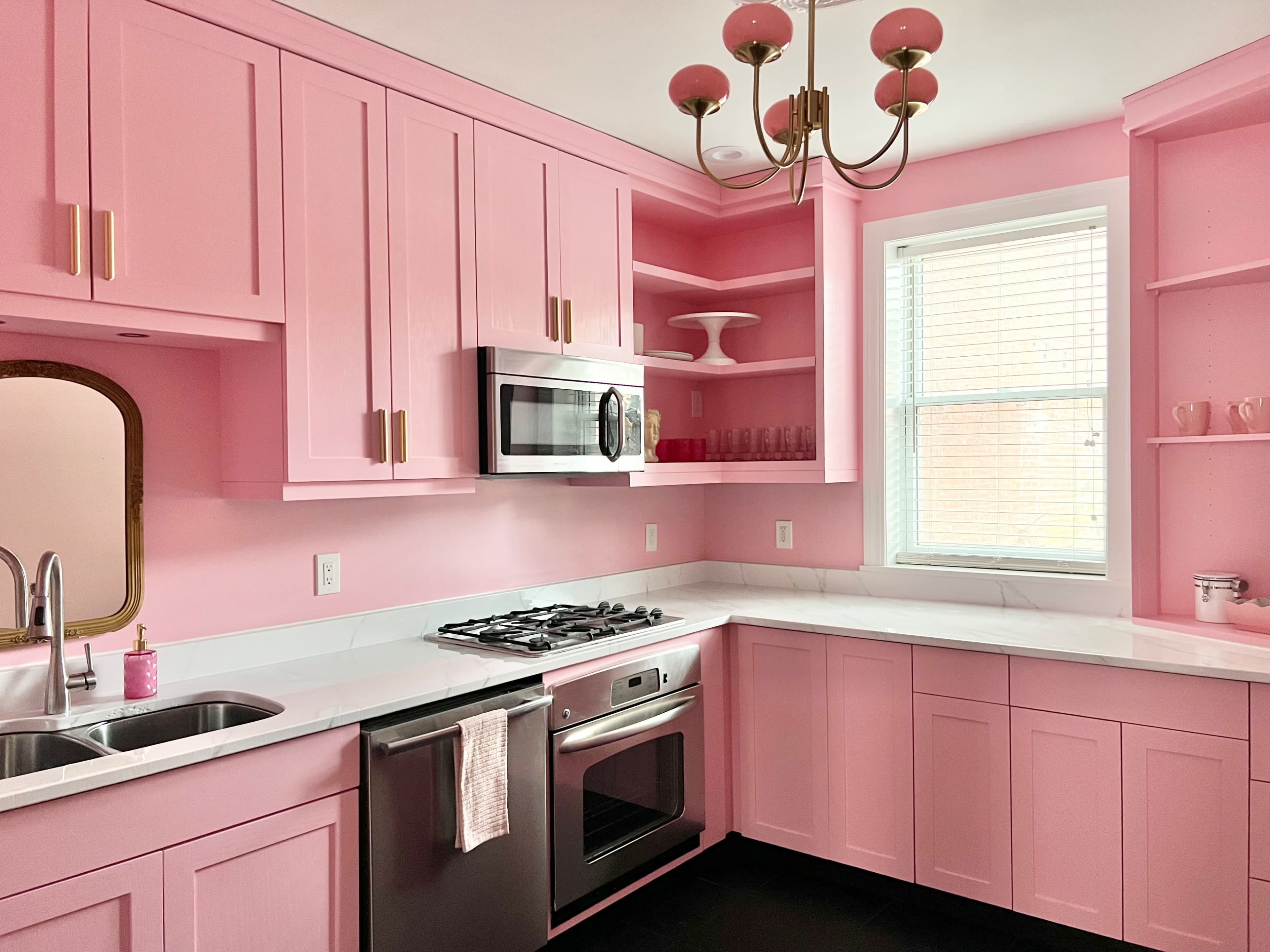 A kitchen with pink cabinets, a silver microwave, and a window illuminating the space.
