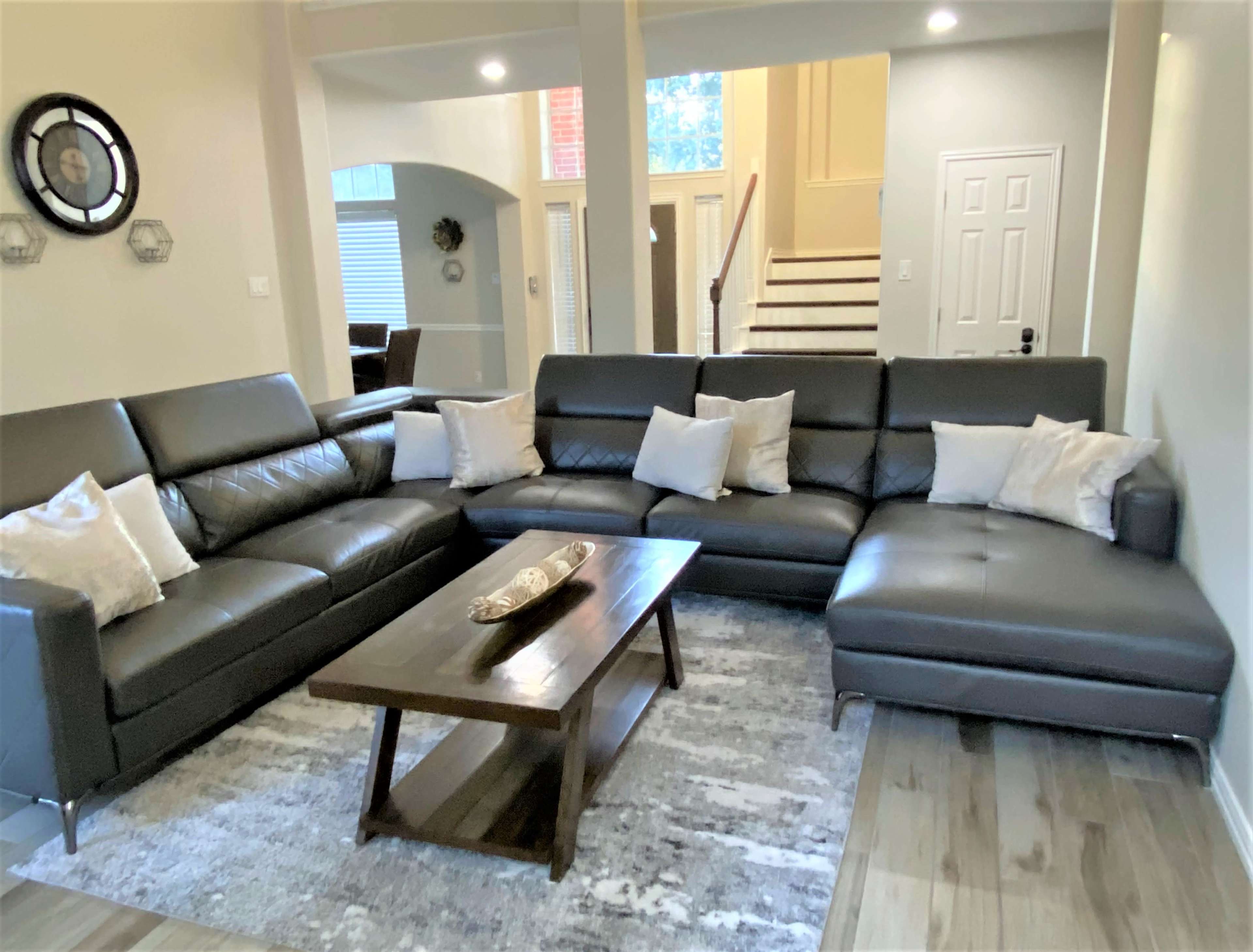 The living room features a large sectional sofa with several cushions, a wooden coffee table, and a rug on the floor.