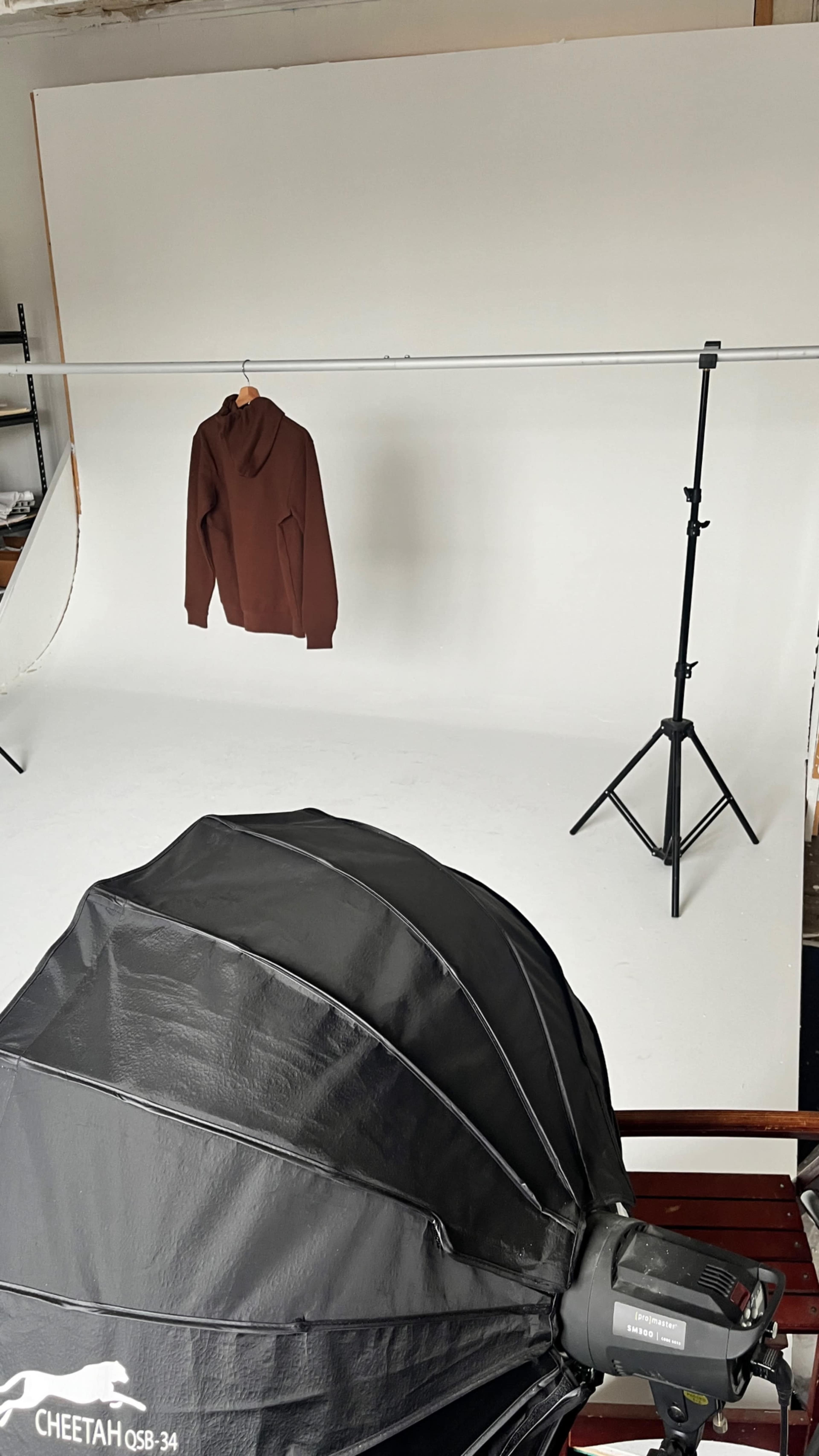 A brown hoodie is suspended in front of a white backdrop, with a photography light umbrella in the foreground.