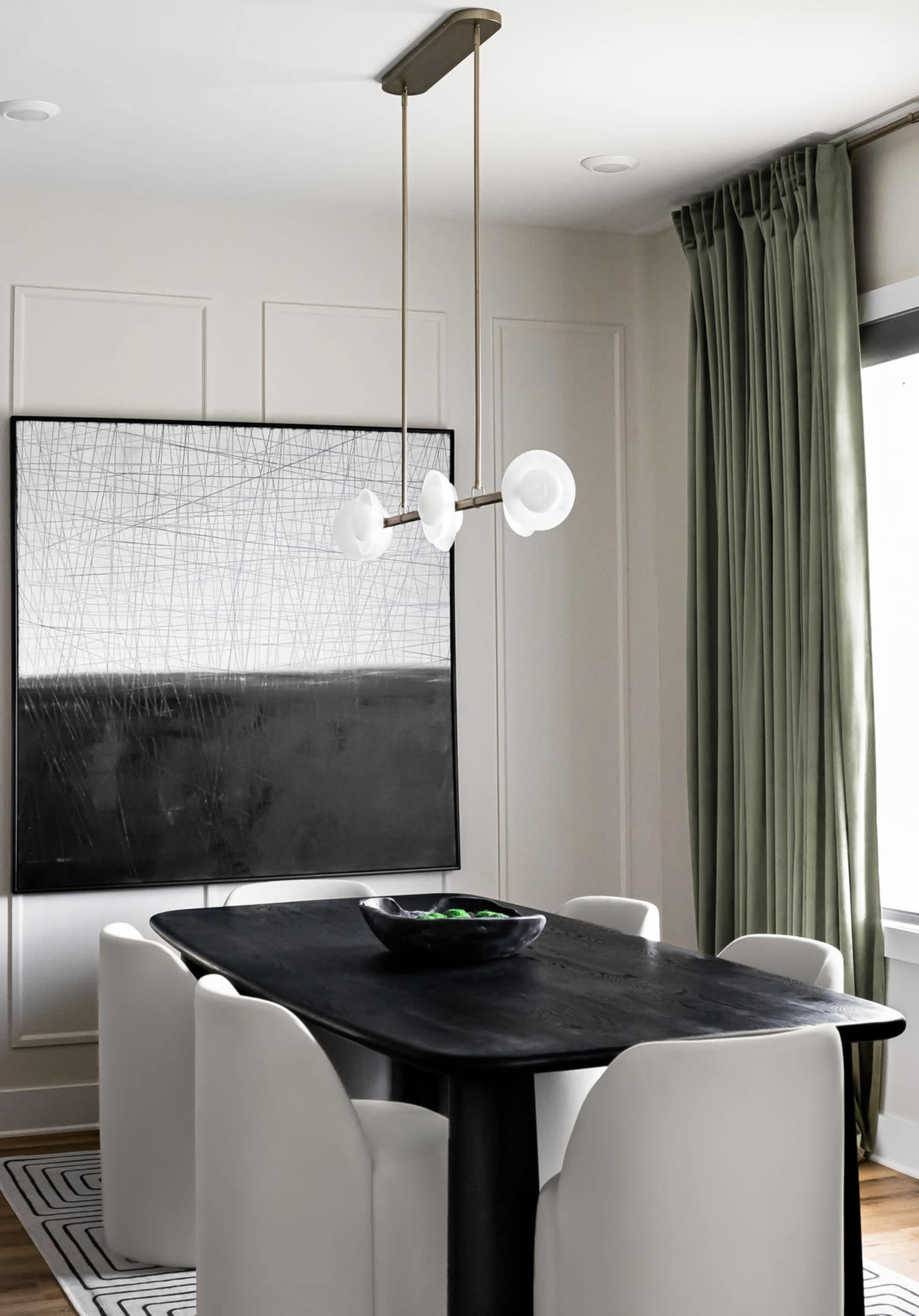 A modern dining room features a black tabletop surrounded by white chairs, a pendant light above, and a large abstract painting on the wall.