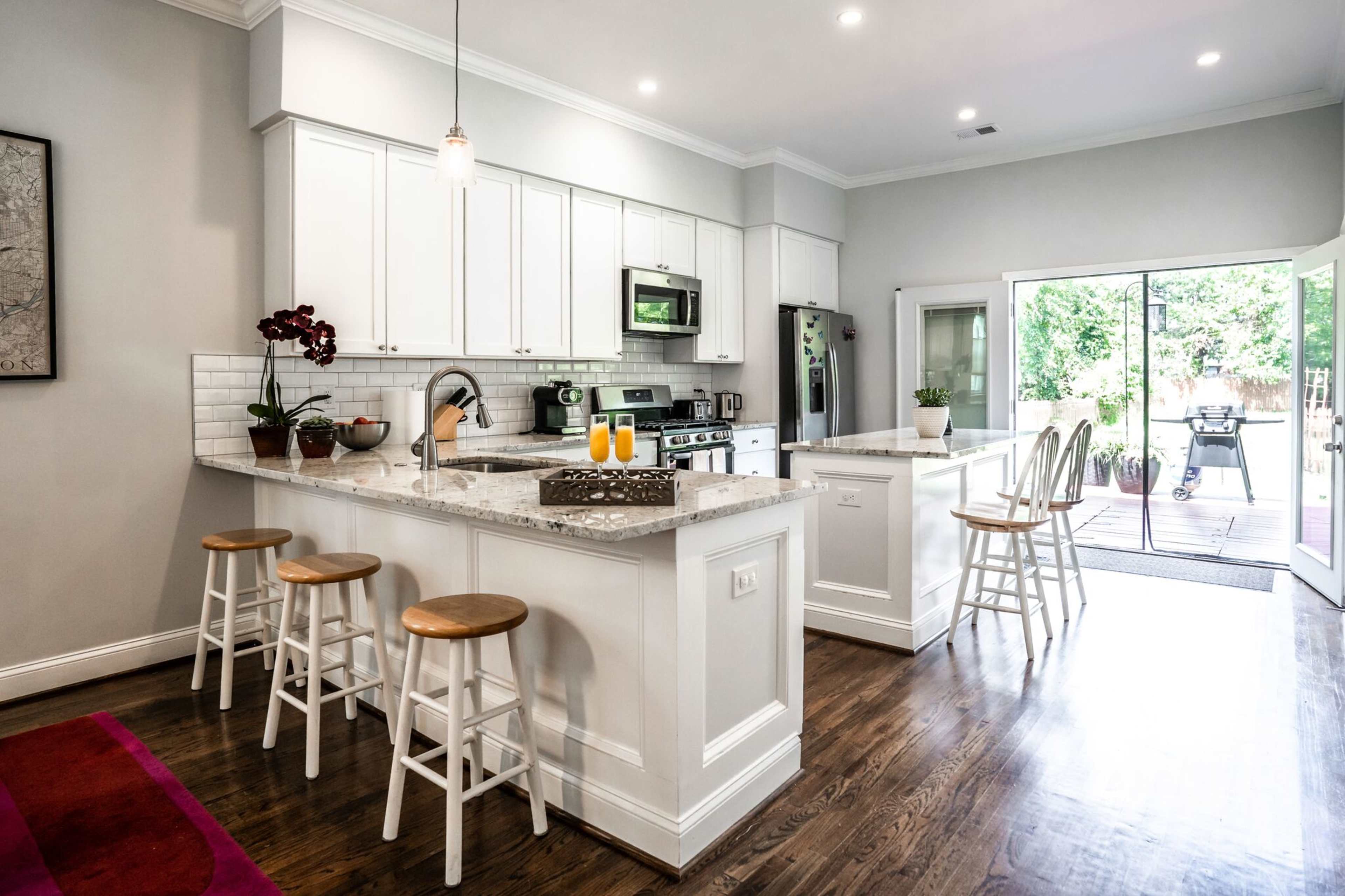 A modern kitchen with white cabinets, stainless steel appliances, a granite countertop island, and a doorway leading to an outdoor patio.