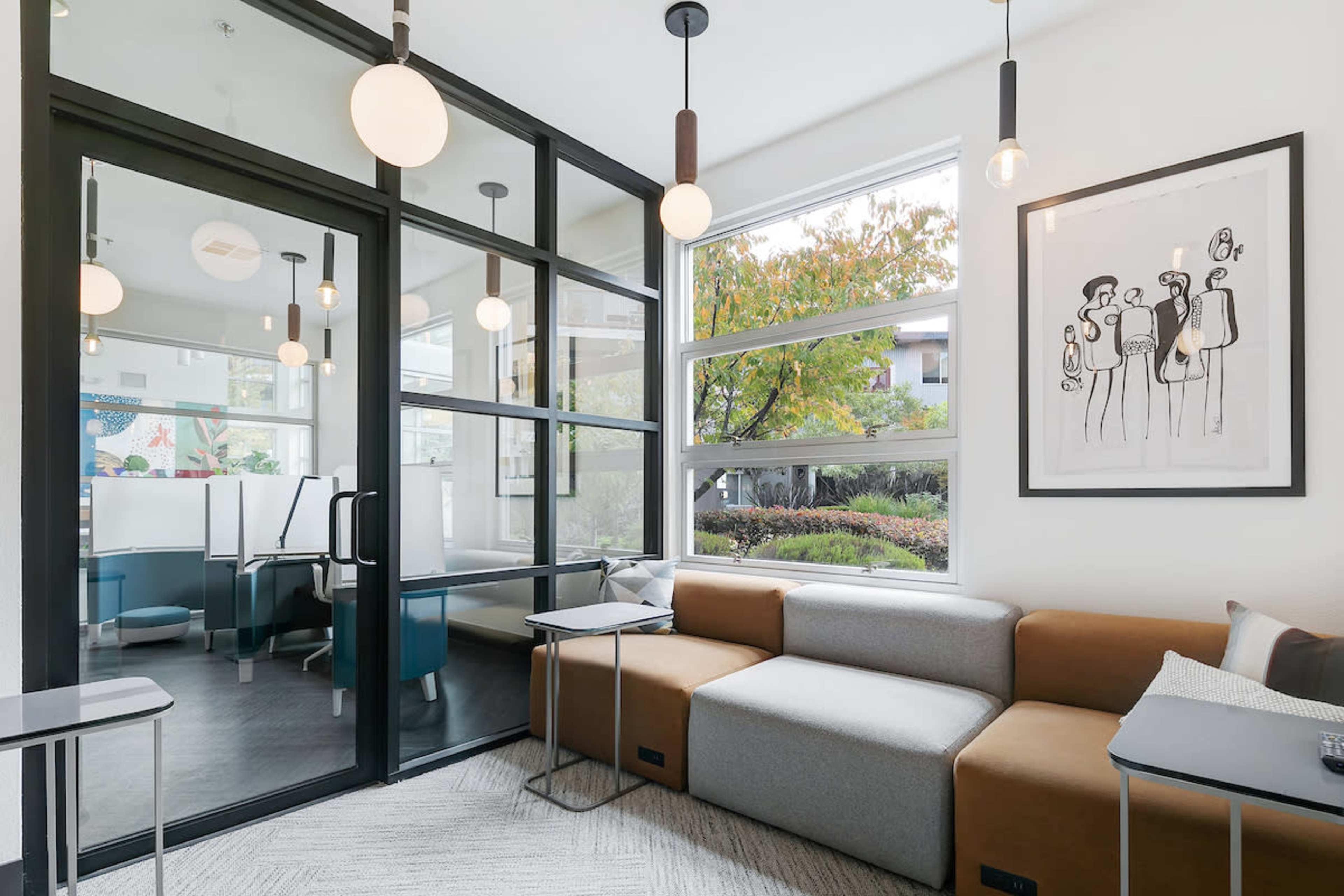 The image shows a modern lounge area with a sectional sofa, large windows, and a glass partition separating it from another room.