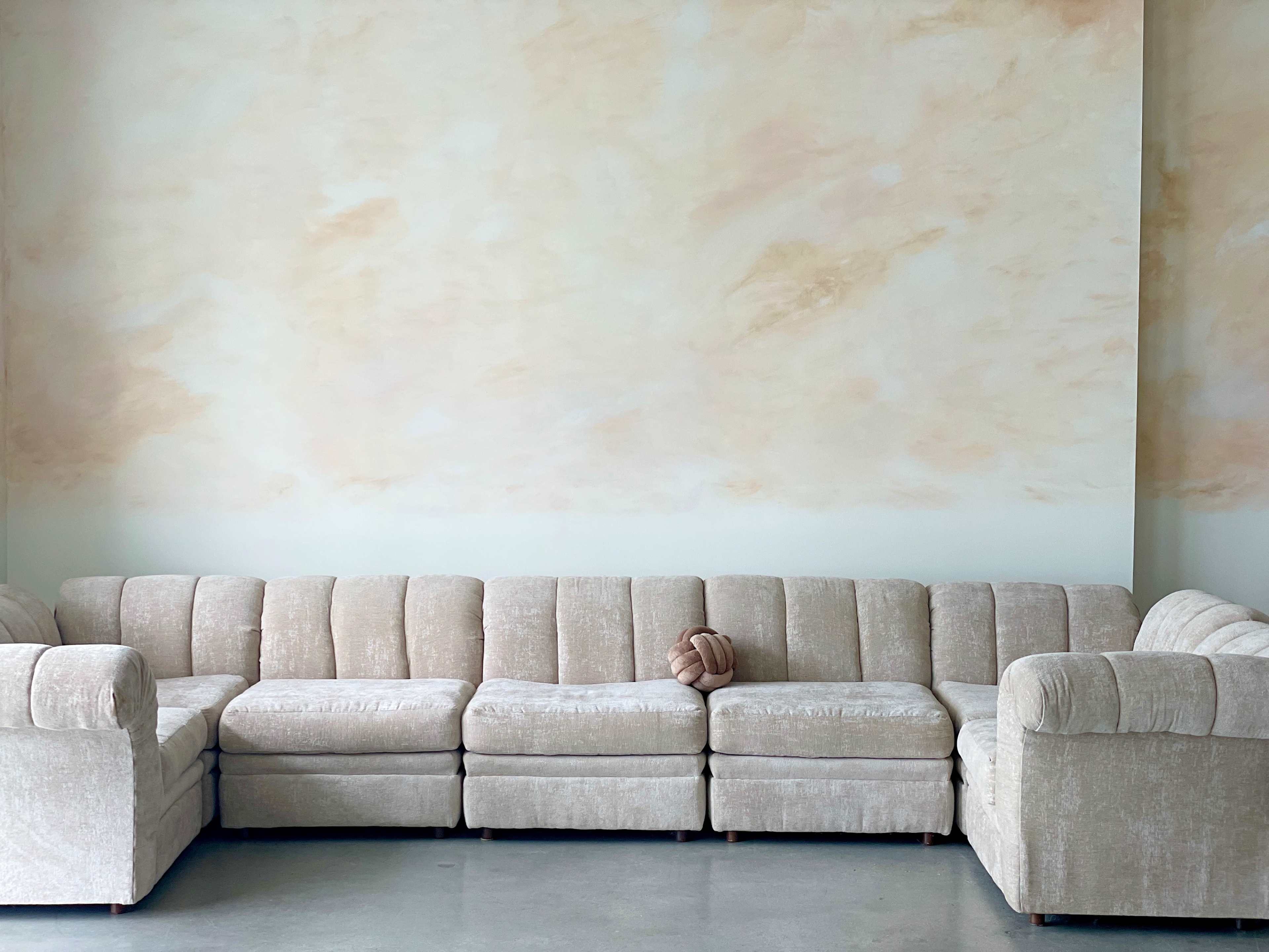 A light-colored sectional sofa is positioned against a softly painted beige wall in a minimalist setting.