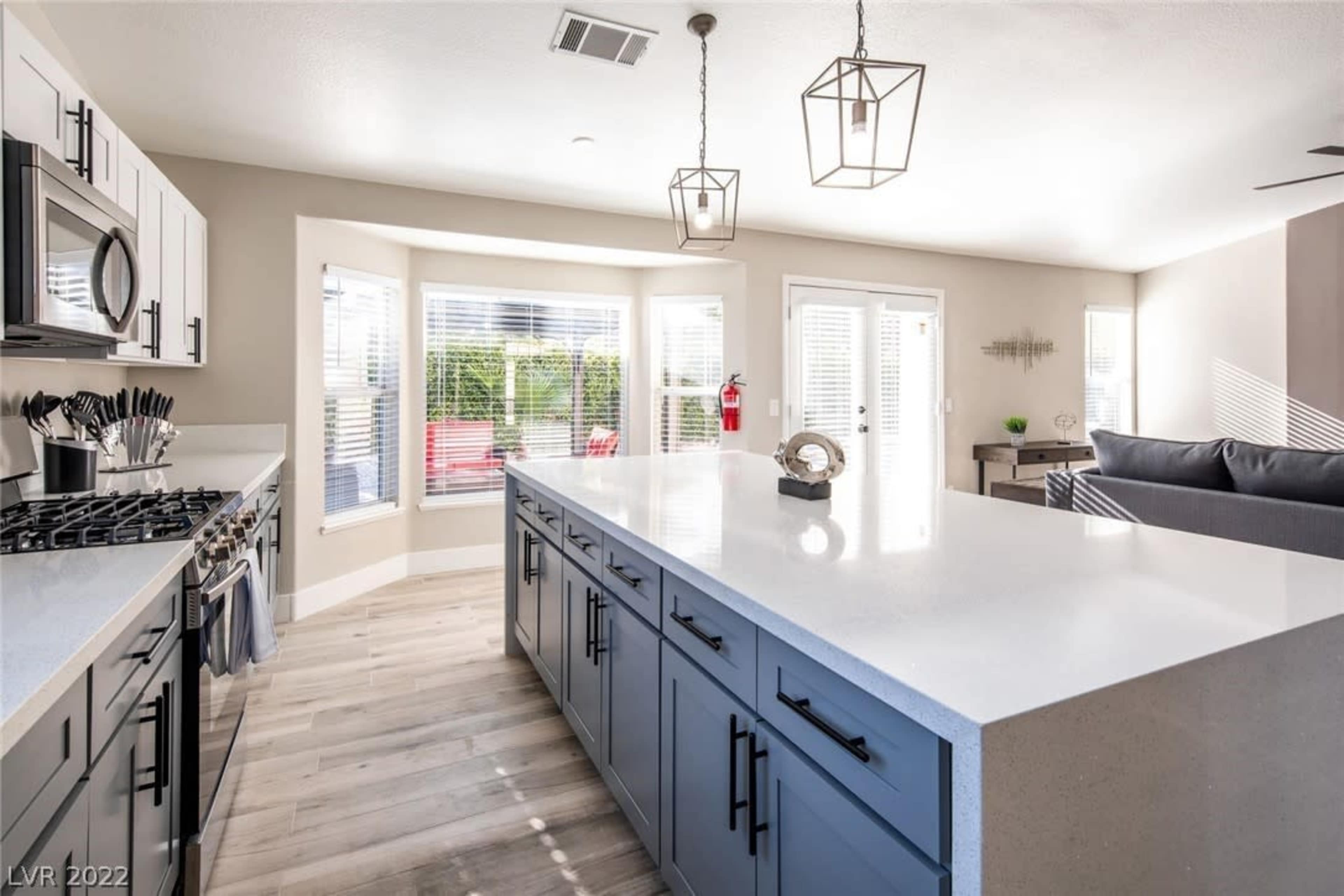 The image shows a modern kitchen with a large island, stainless steel appliances, and a dining area featuring a bay window.