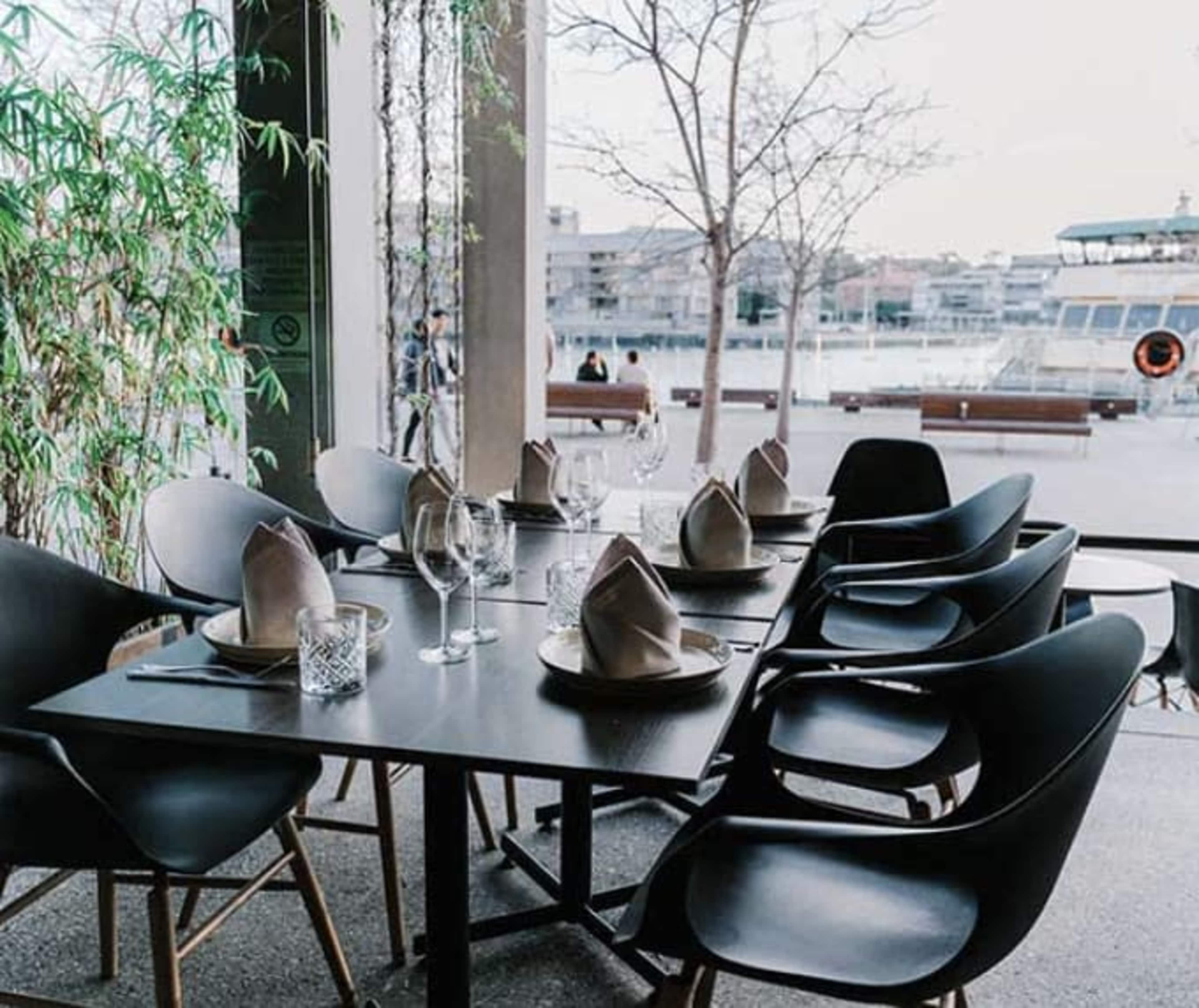 A dining table set with glassware and folded napkins in a restaurant overlooking a waterfront view.