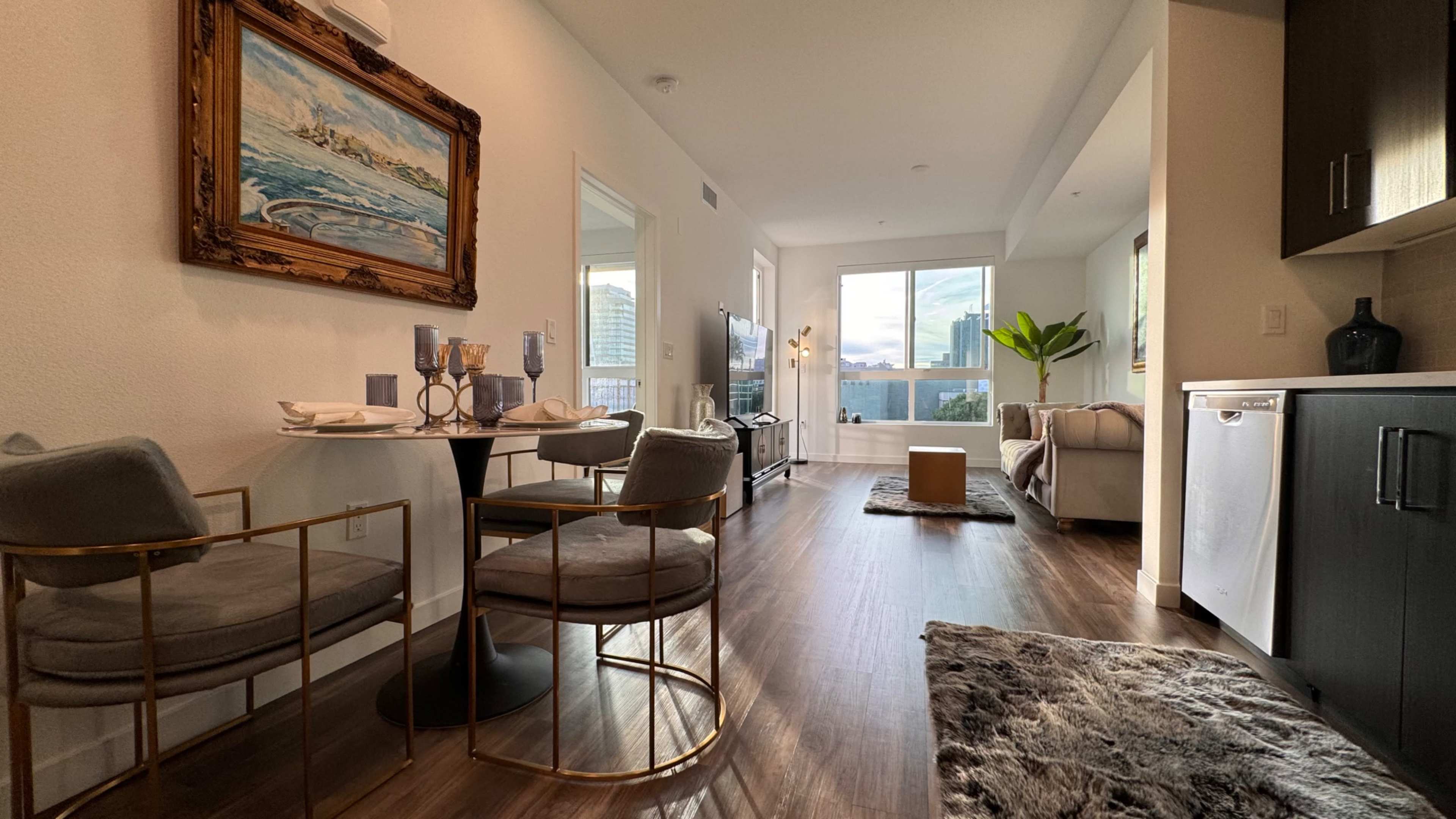 A modern living space featuring a dining area with a round table and chairs, a cozy sofa, and large windows allowing natural light.
