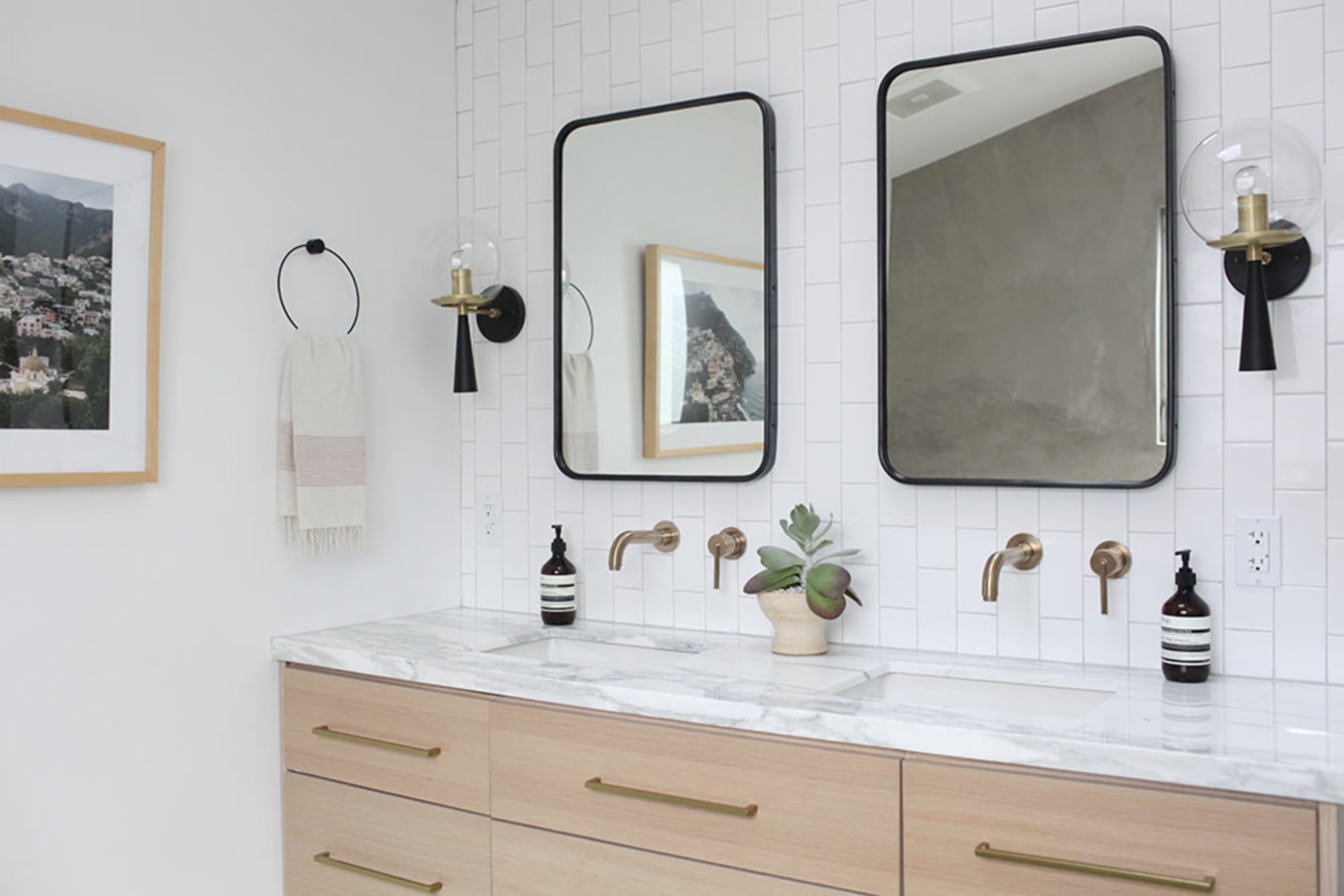 A modern bathroom with two wall-mounted mirrors above a marble countertop, featuring dual faucets and a minimalistic wooden vanity.