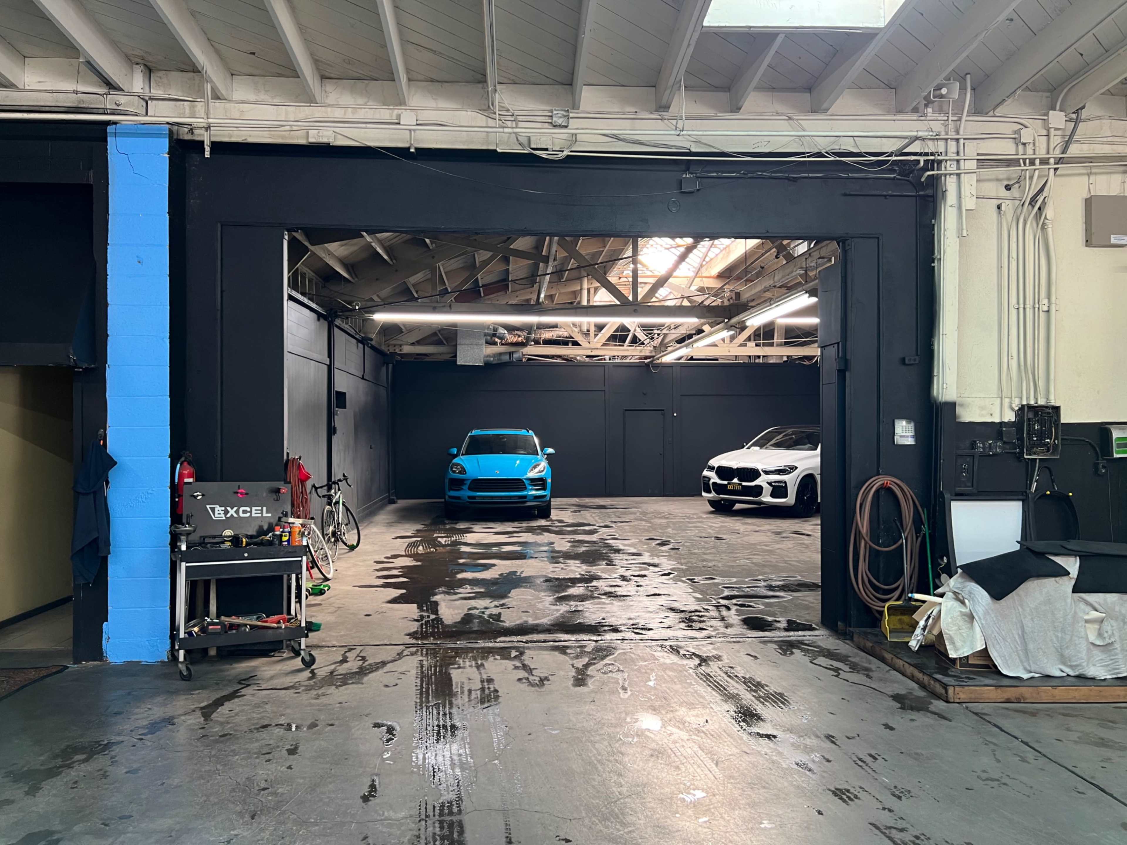 A blue sports car and a white sedan are parked in a spacious garage with a polished concrete floor.