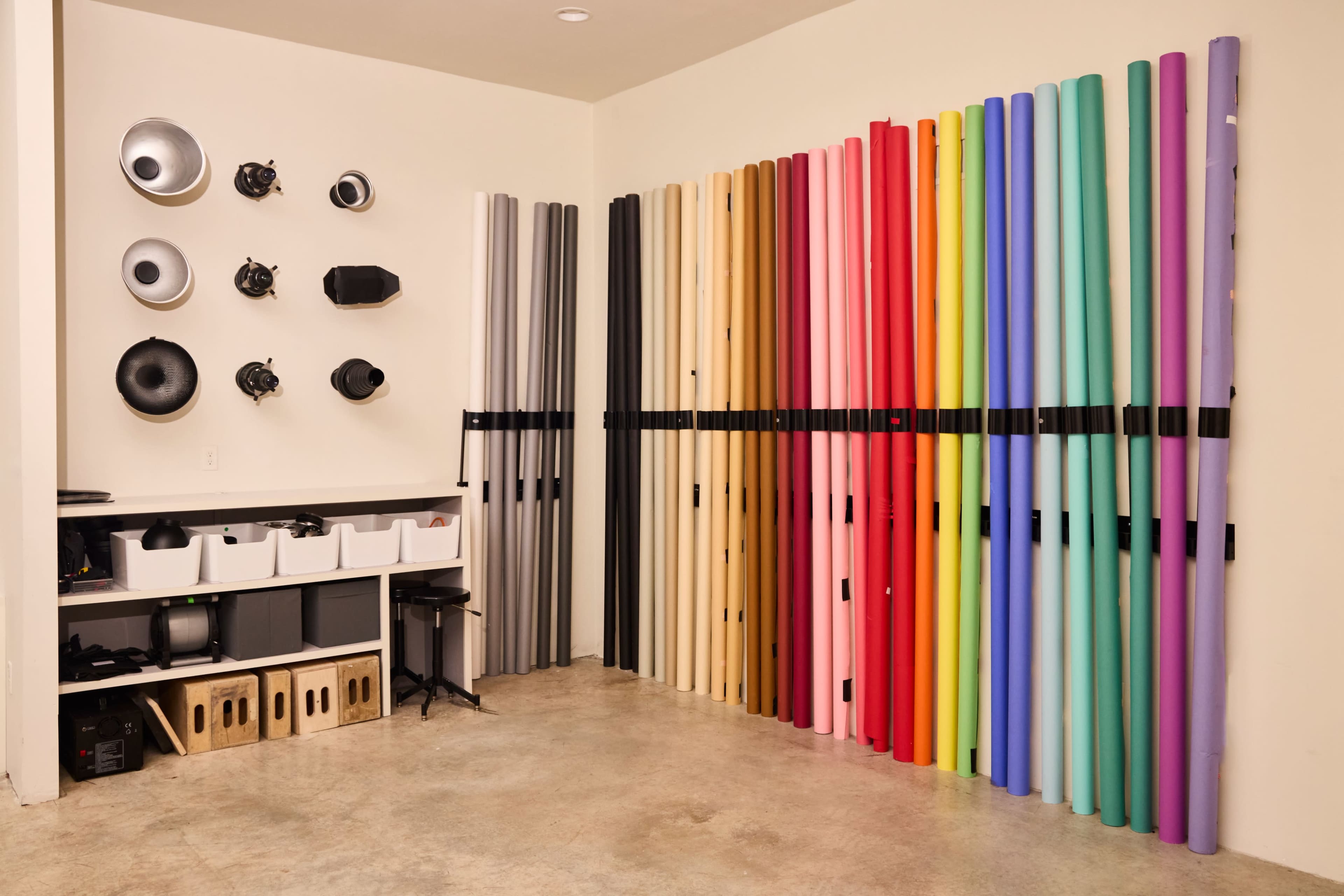 A studio space with various colored backdrop rolls against a wall and lighting equipment mounted above.