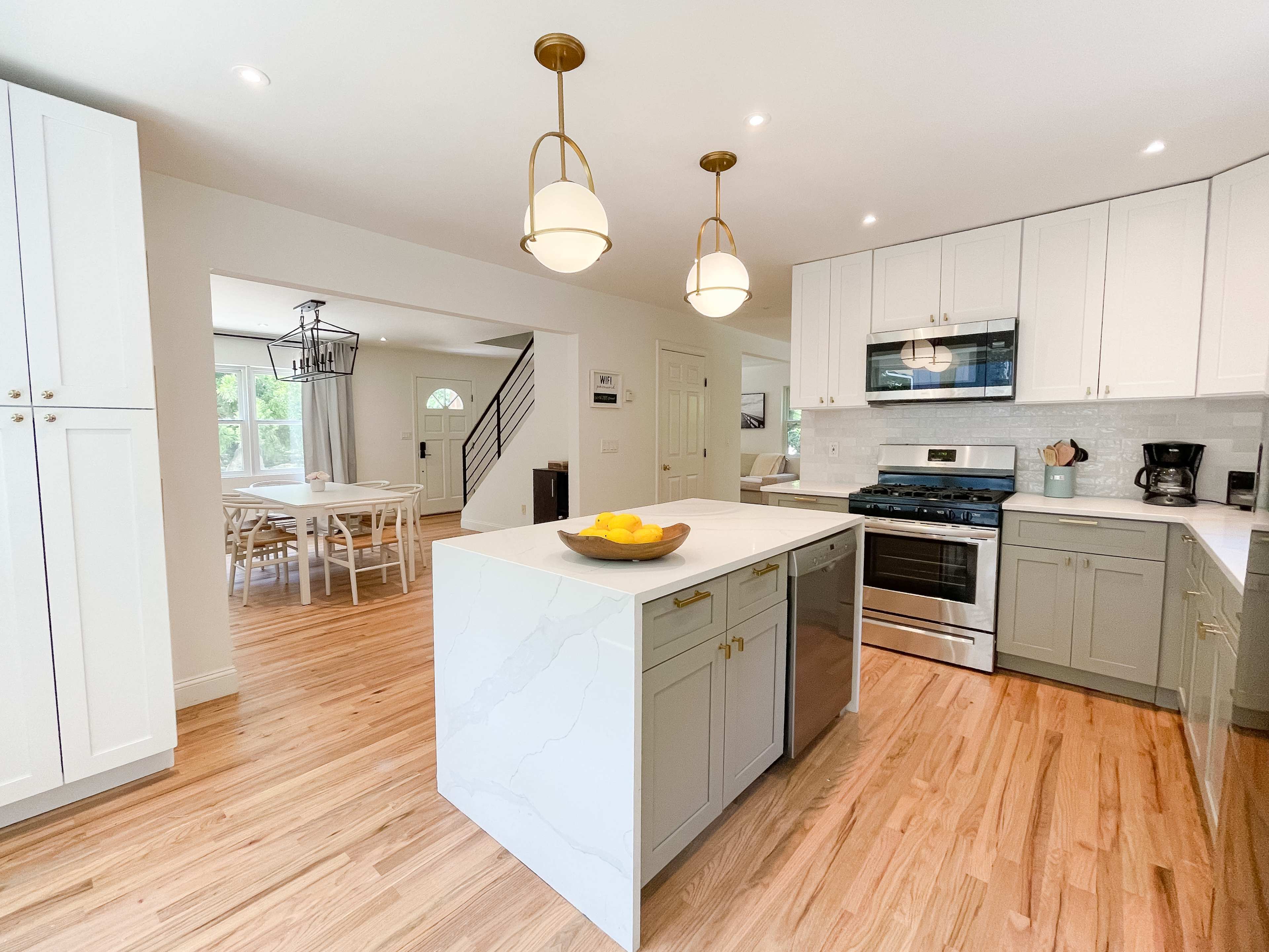 A bright kitchen with an island that has a bowl of lemons, modern appliances, and white cabinetry.