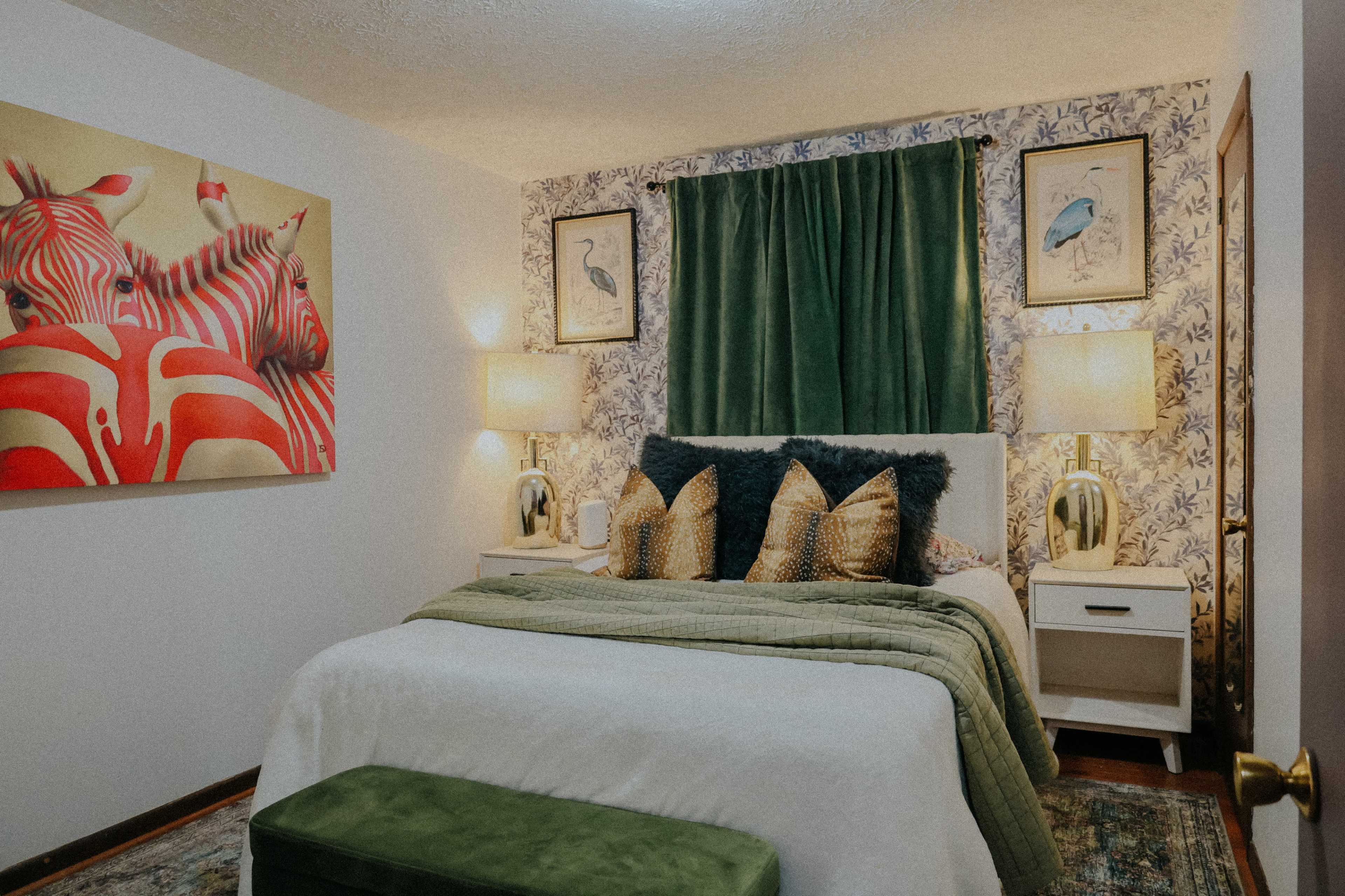 The image shows a cozy bedroom featuring a bed with green and white bedding, decorative pillows, and walls adorned with a zebra-themed painting and floral wallpaper.