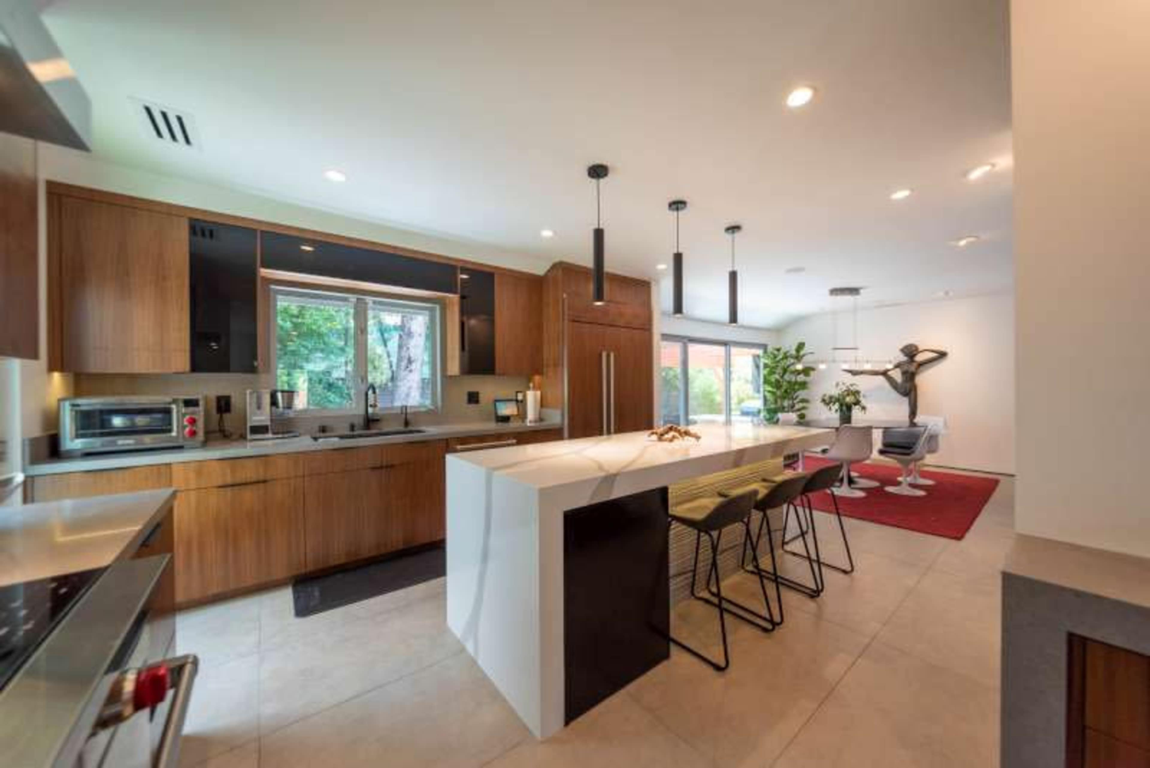 A modern kitchen with wooden cabinetry, an island countertop, and a dining area featuring a white table and chairs.