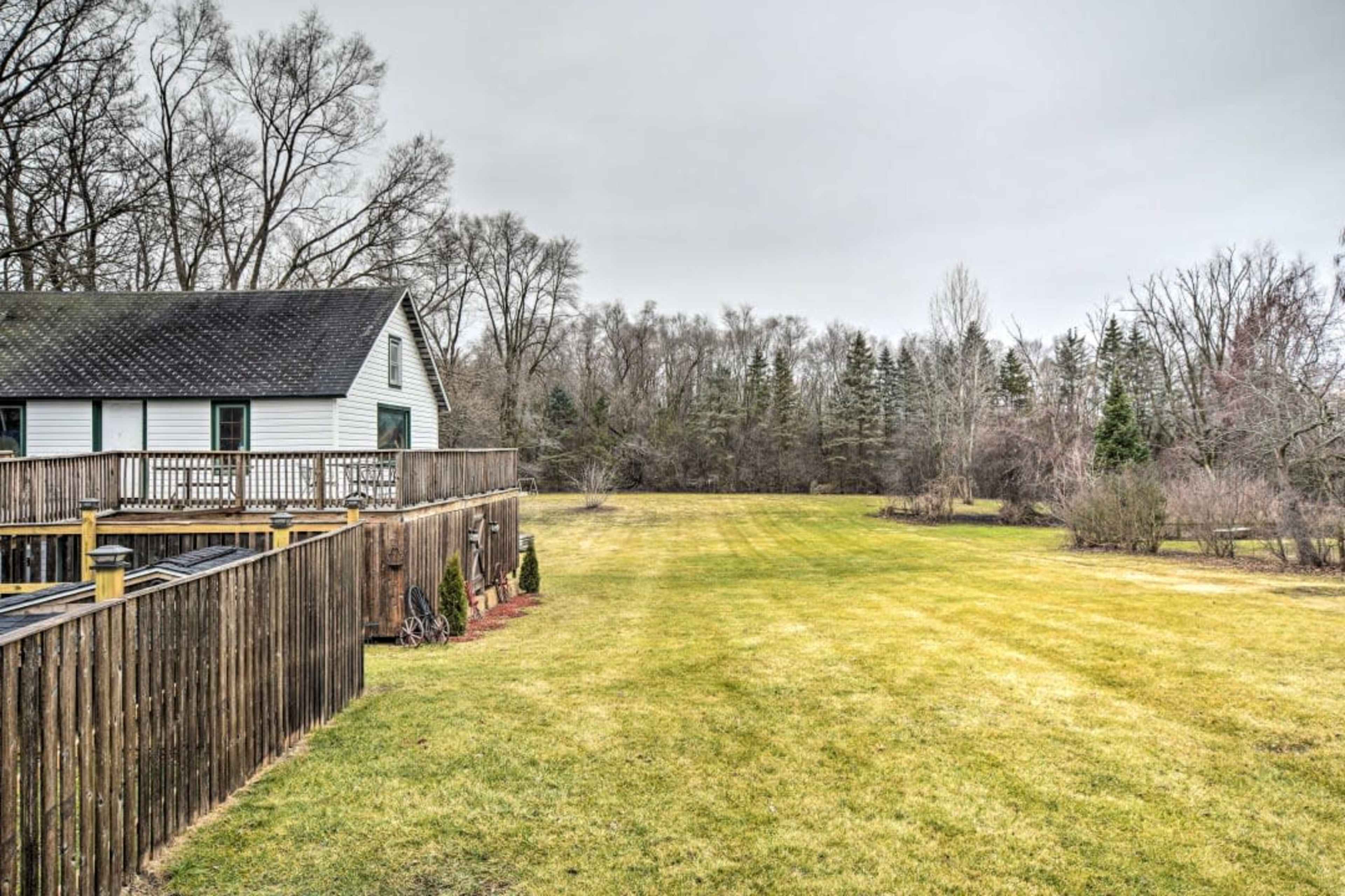 A grassy lawn extends behind a white house, bordered by a wooden fence and flanked by trees in the background.