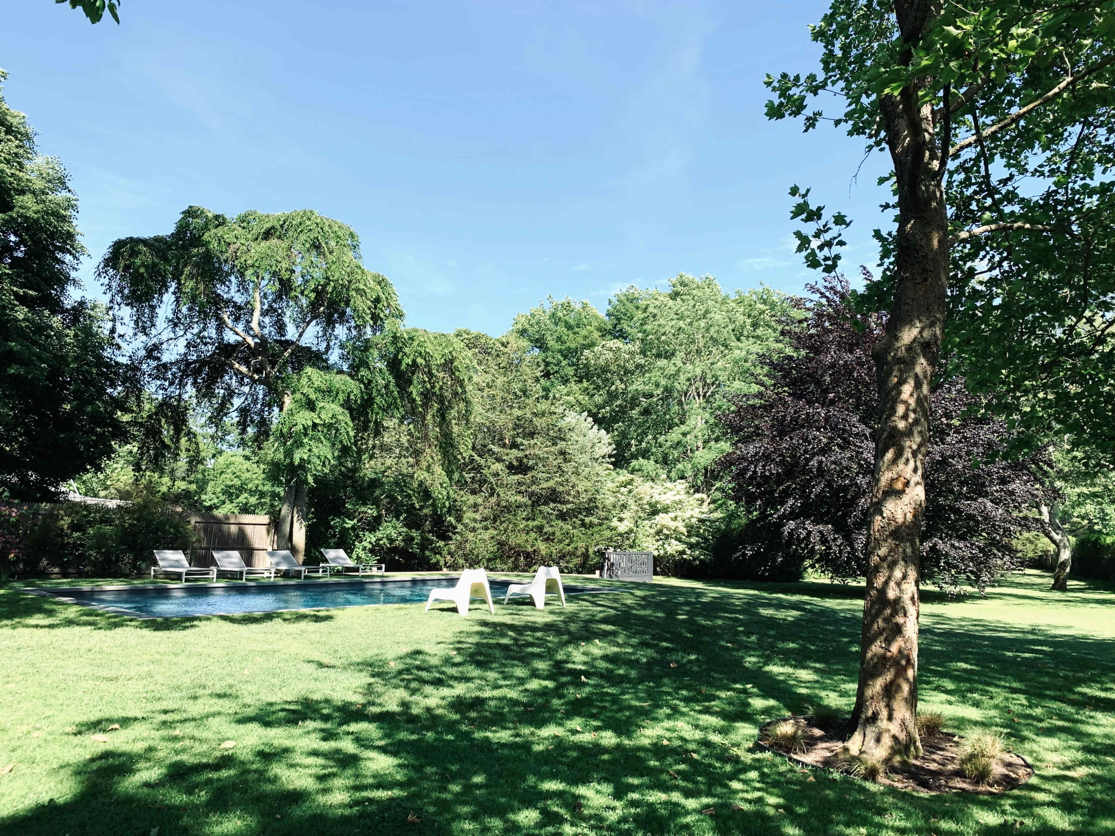 A swimming pool surrounded by lush green grass and various trees is visible in the scene.