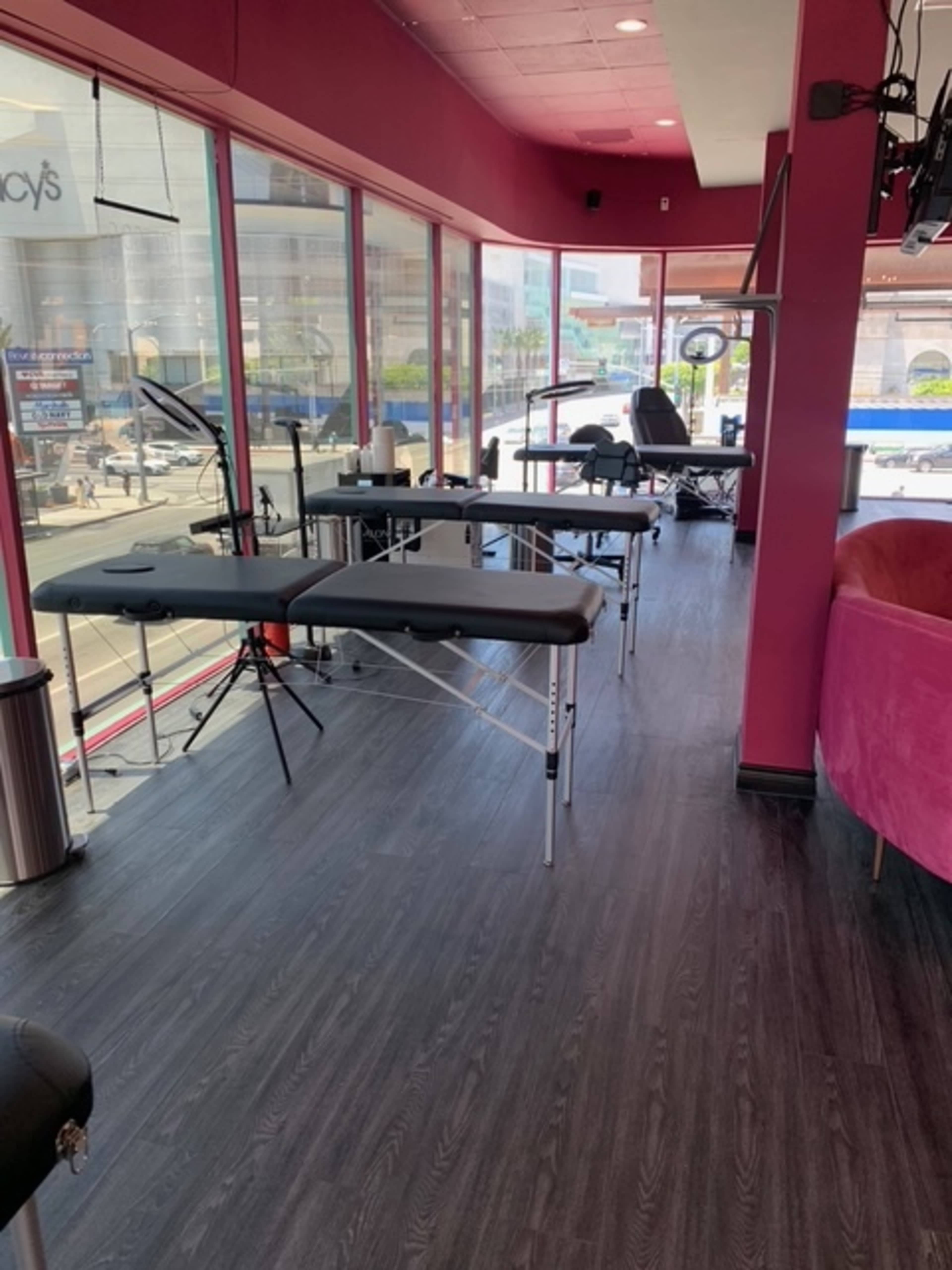 The image shows a brightly lit salon interior with multiple massage tables set up along large windows, revealing a view of the street outside.