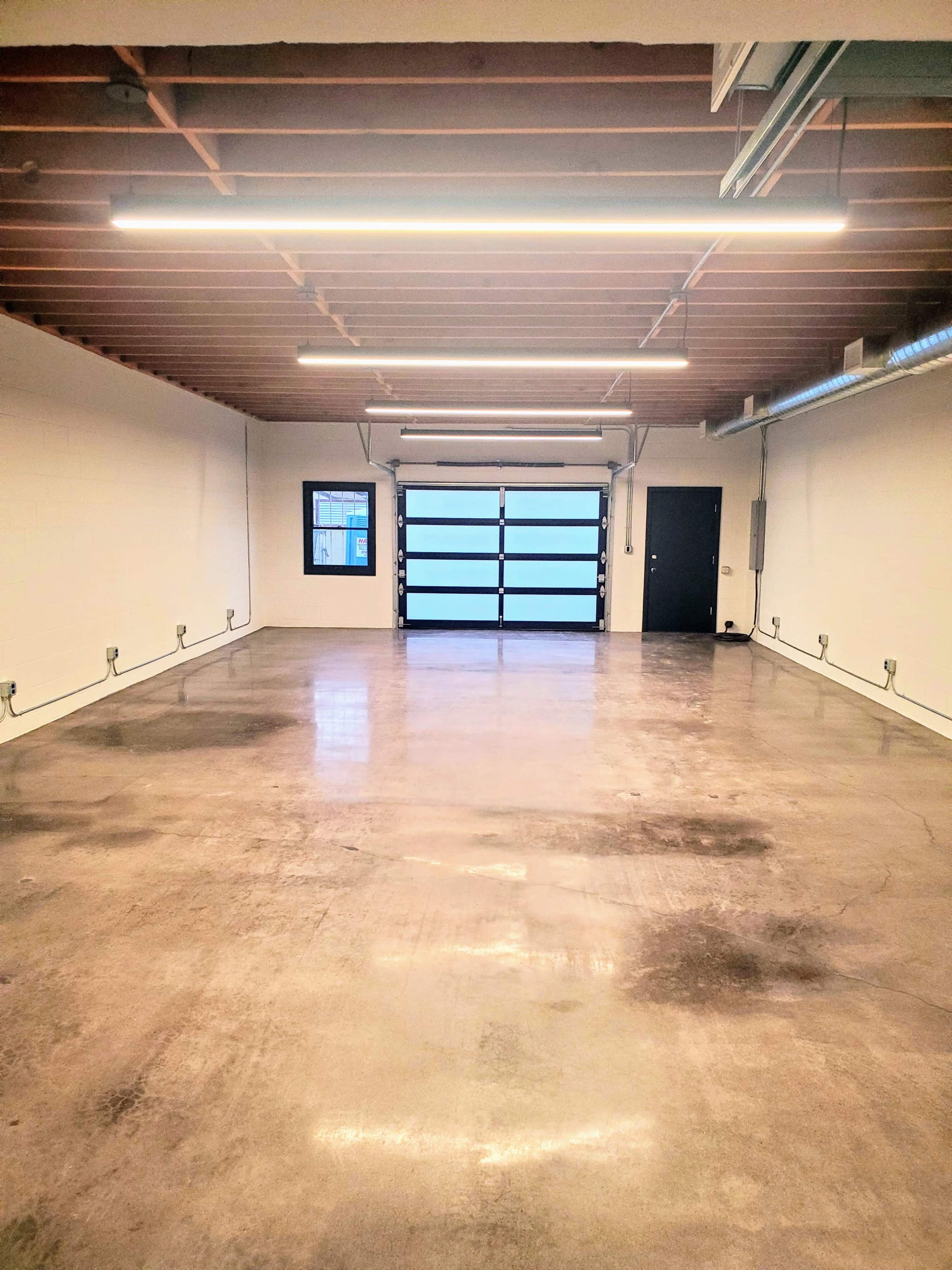 The image shows a spacious, empty garage with concrete flooring and large glass doors at the front.