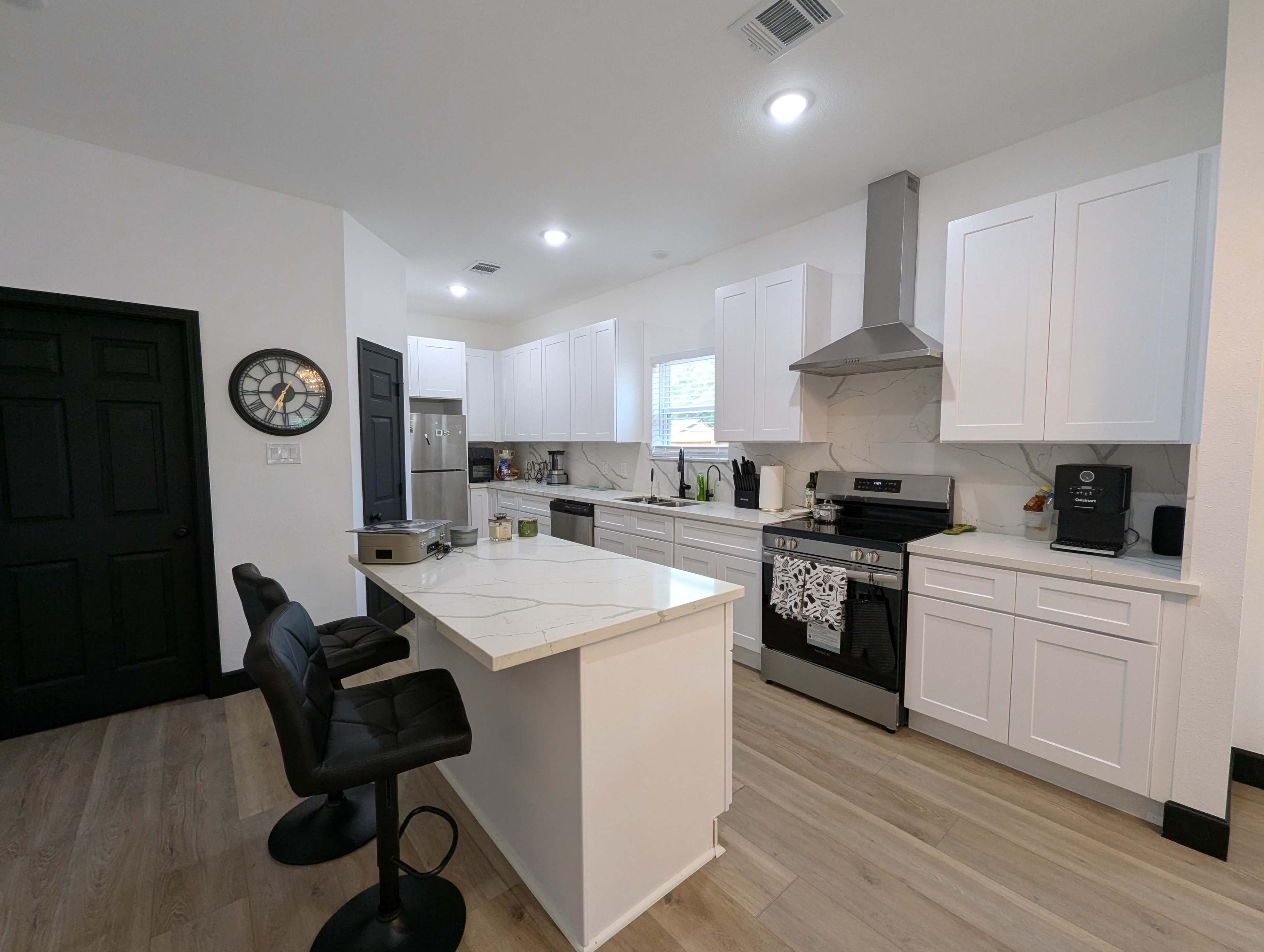 The image shows a modern kitchen with white cabinetry, a large island with bar stools, and stainless steel appliances.