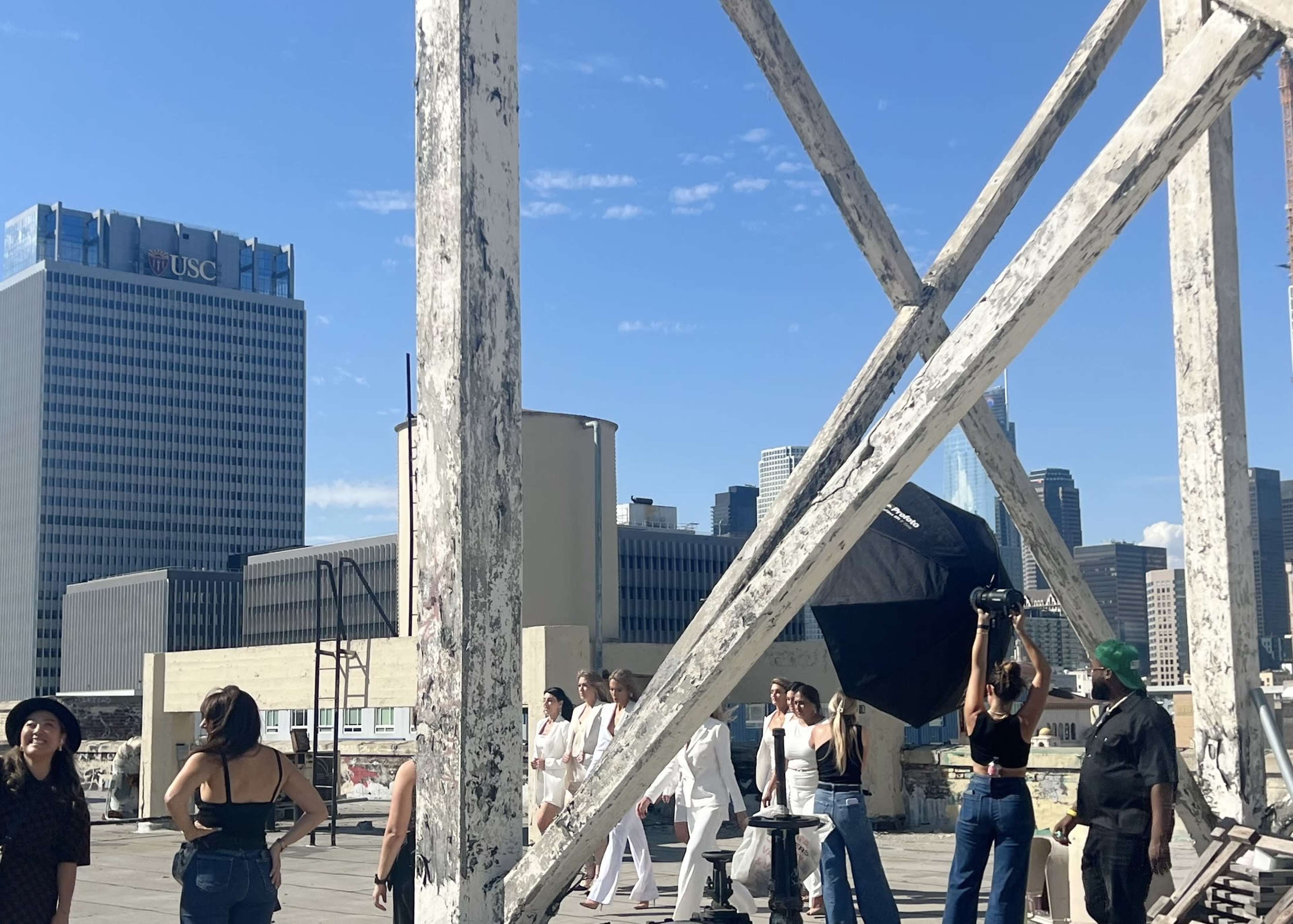 A group of people is gathered on a rooftop, with some posing for a photoshoot against a backdrop of downtown buildings.